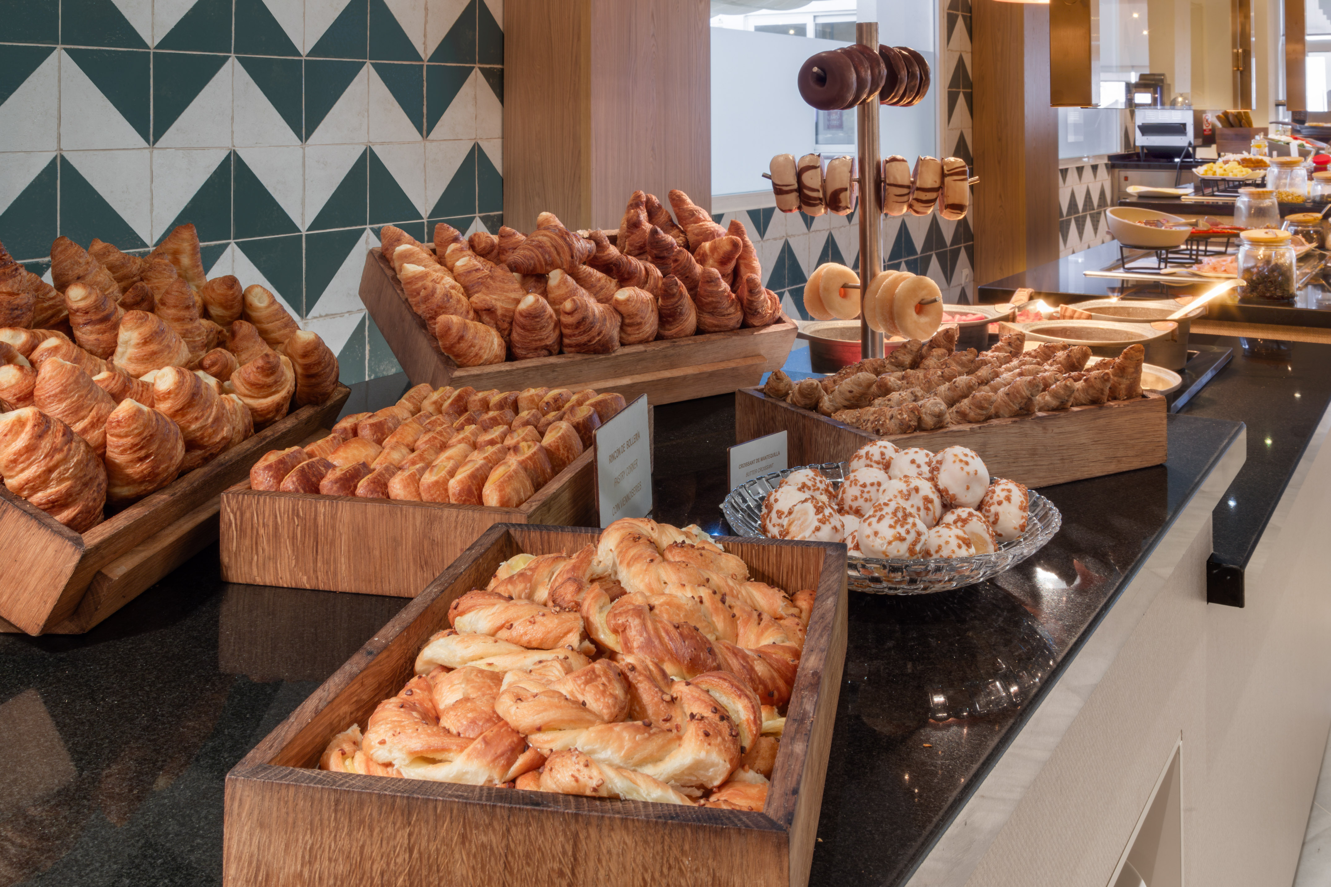 Hotel breakfast buffet with golden croissants, assorted pastries, and donuts.