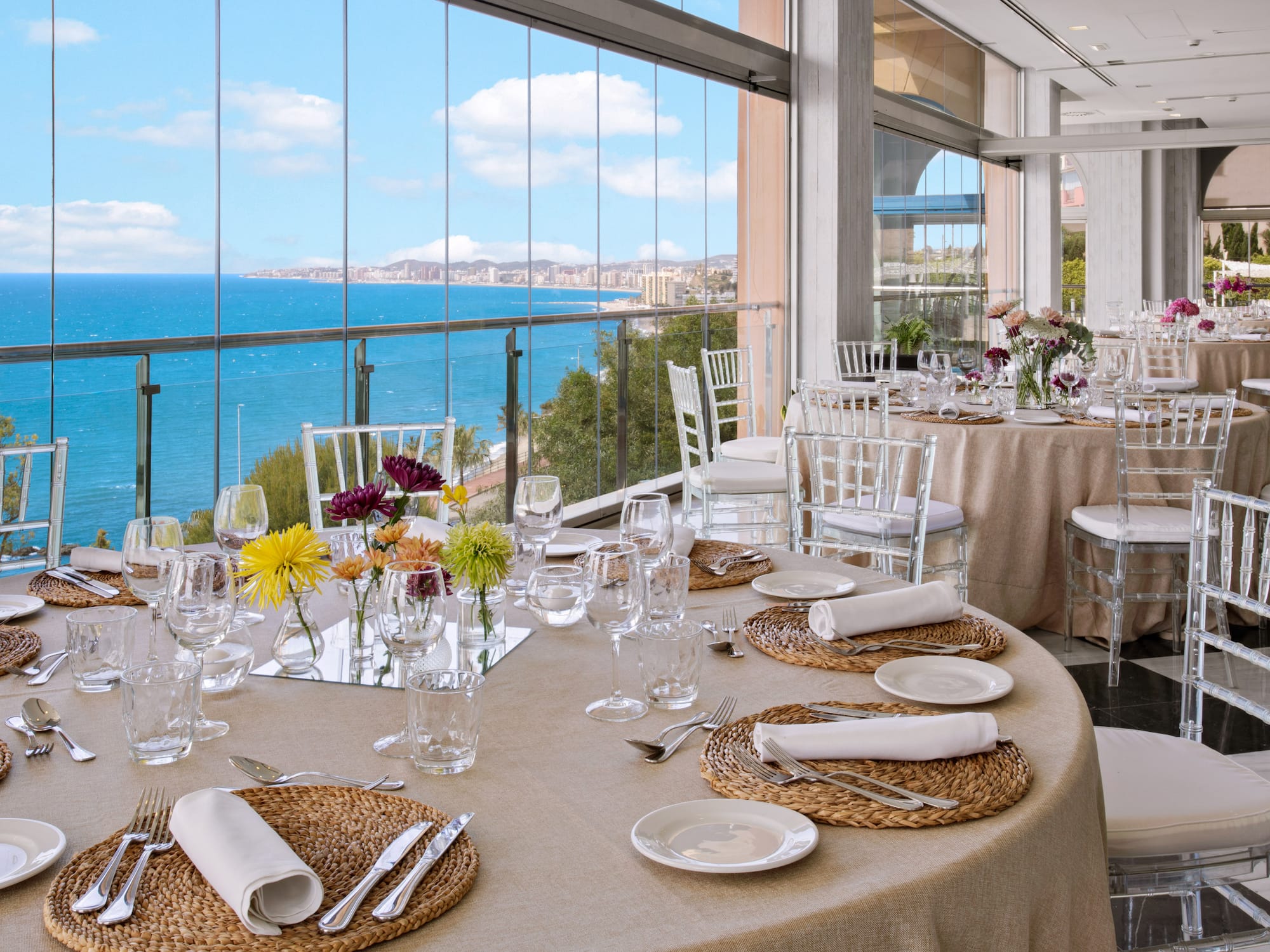 Luxury banquet hall with set tables, floral decor, and panoramic ocean views.