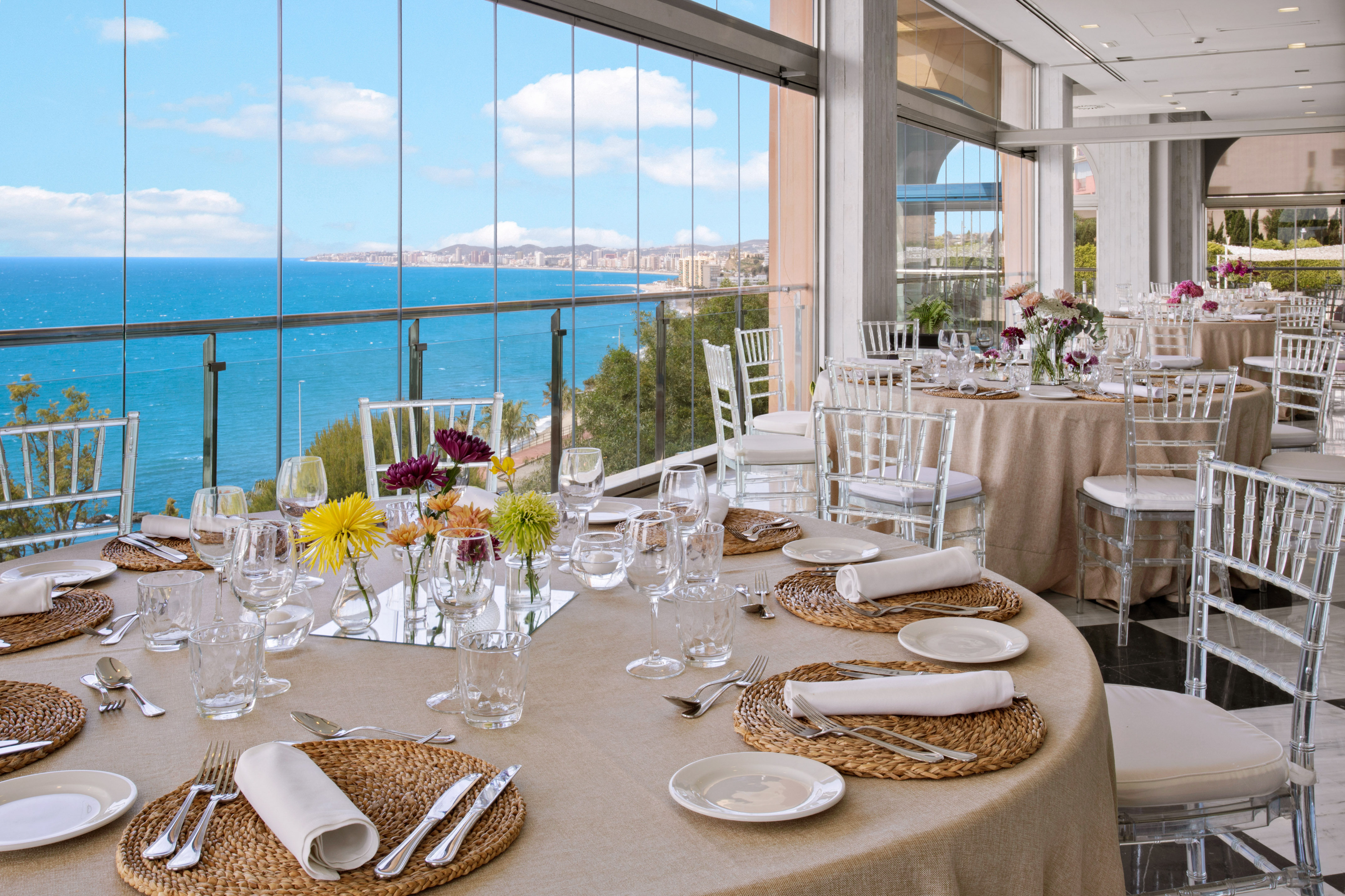 Luxury banquet hall with set tables, floral decor, and panoramic ocean views.