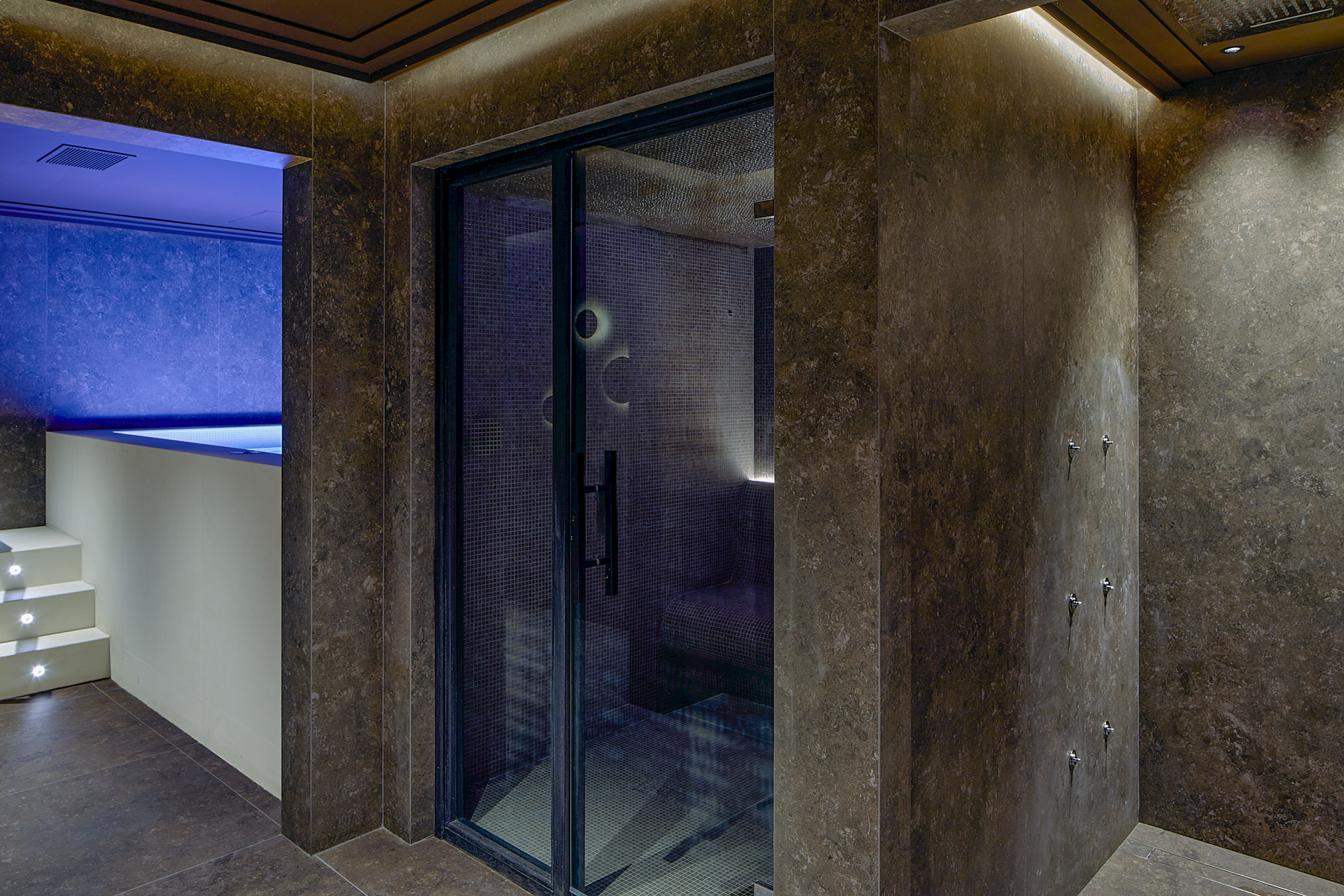 Dark tiled spa featuring a steam room, cool blue plunge pool, and wall showers.
