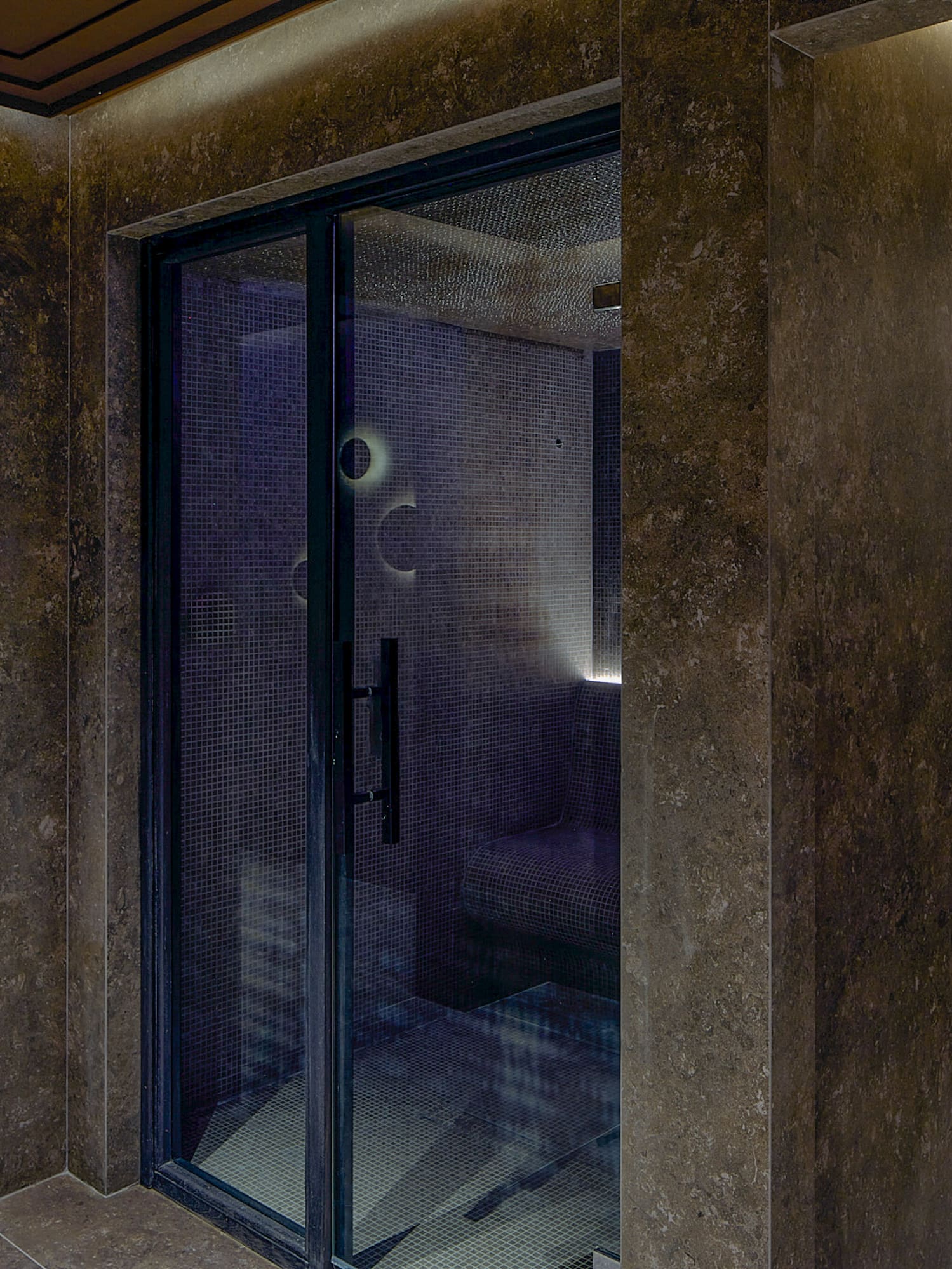 Dark tiled spa featuring a steam room, cool blue plunge pool, and wall showers.