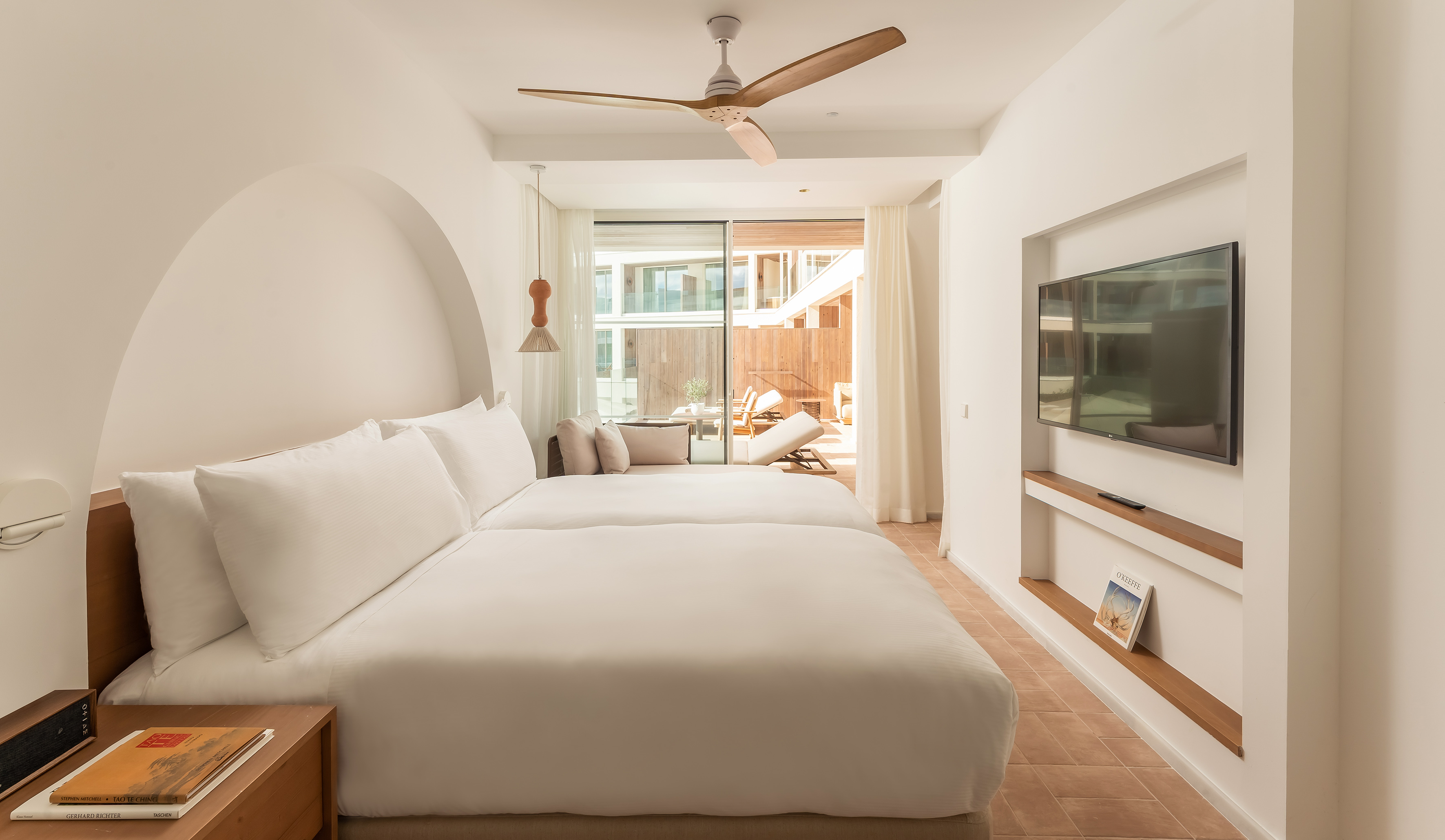 Modern hotel bedroom with white twin beds, ceiling fan, TV, and private patio.