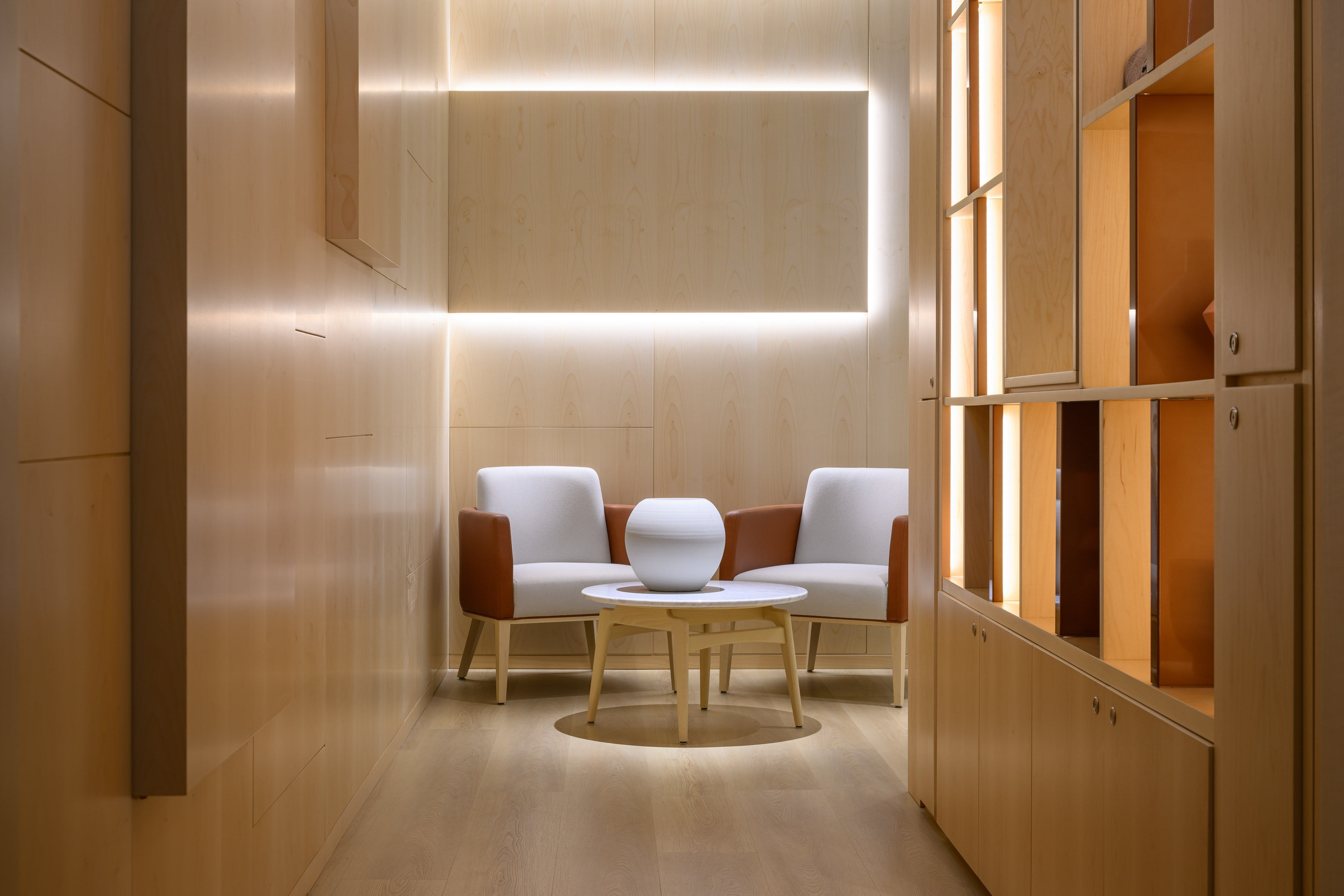 Modern wood lounge with two armchairs, coffee table, and linear lighting.