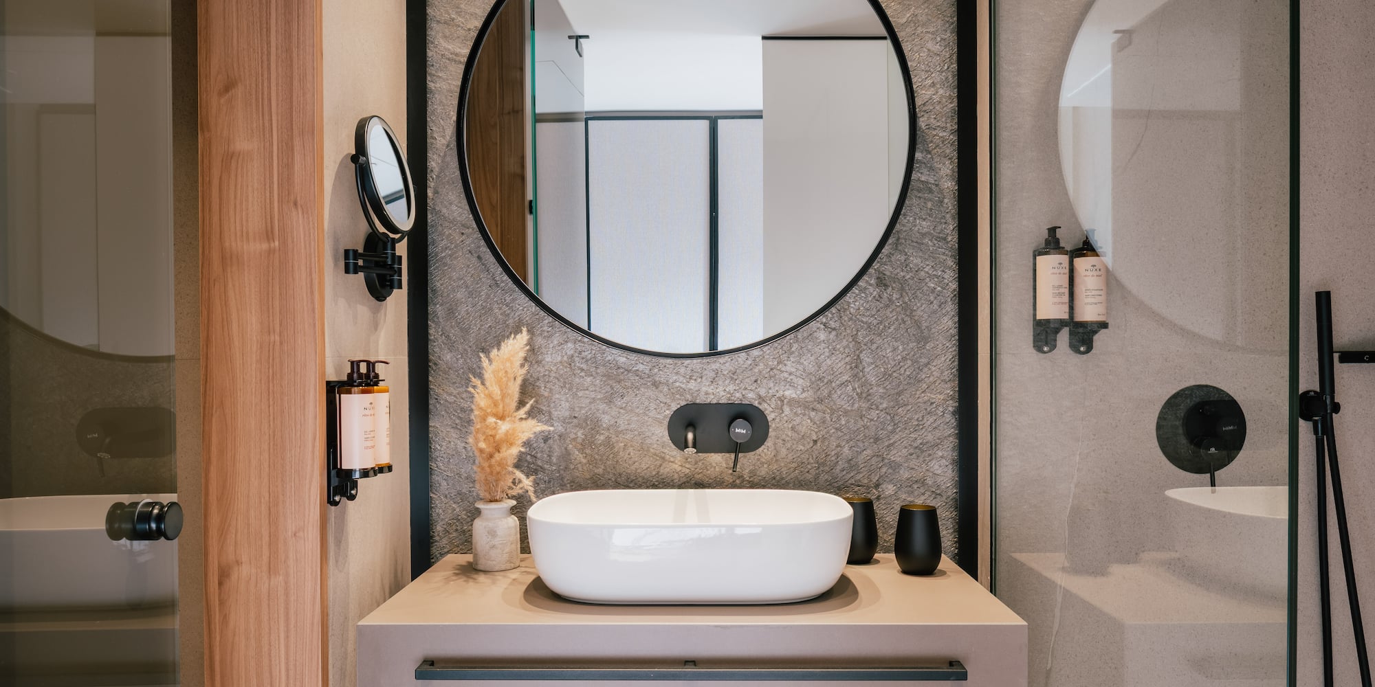 Sleek bathroom vanity, round mirror, white vessel sink, black faucet, stone wall.