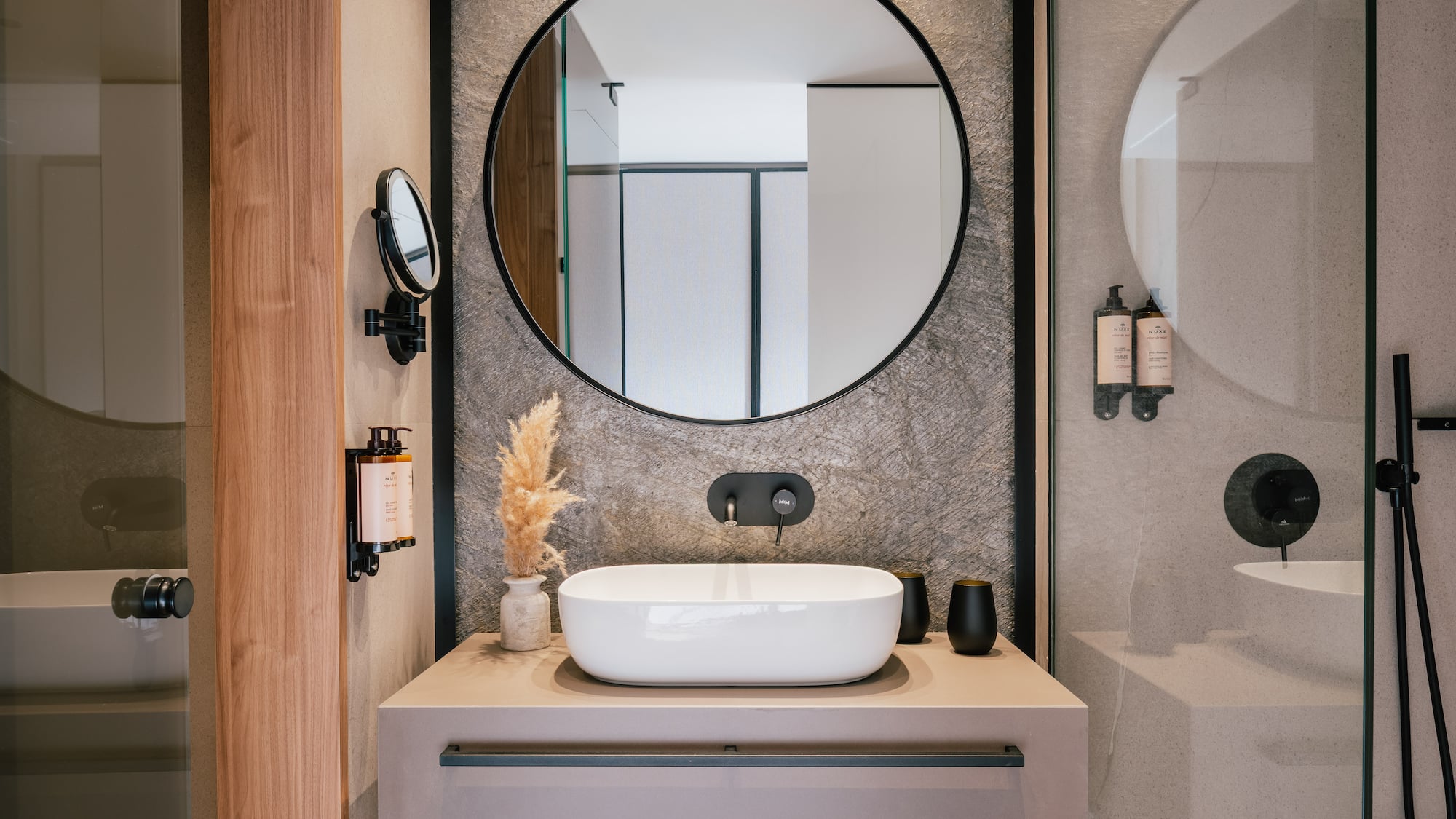 Sleek bathroom vanity, round mirror, white vessel sink, black faucet, stone wall.