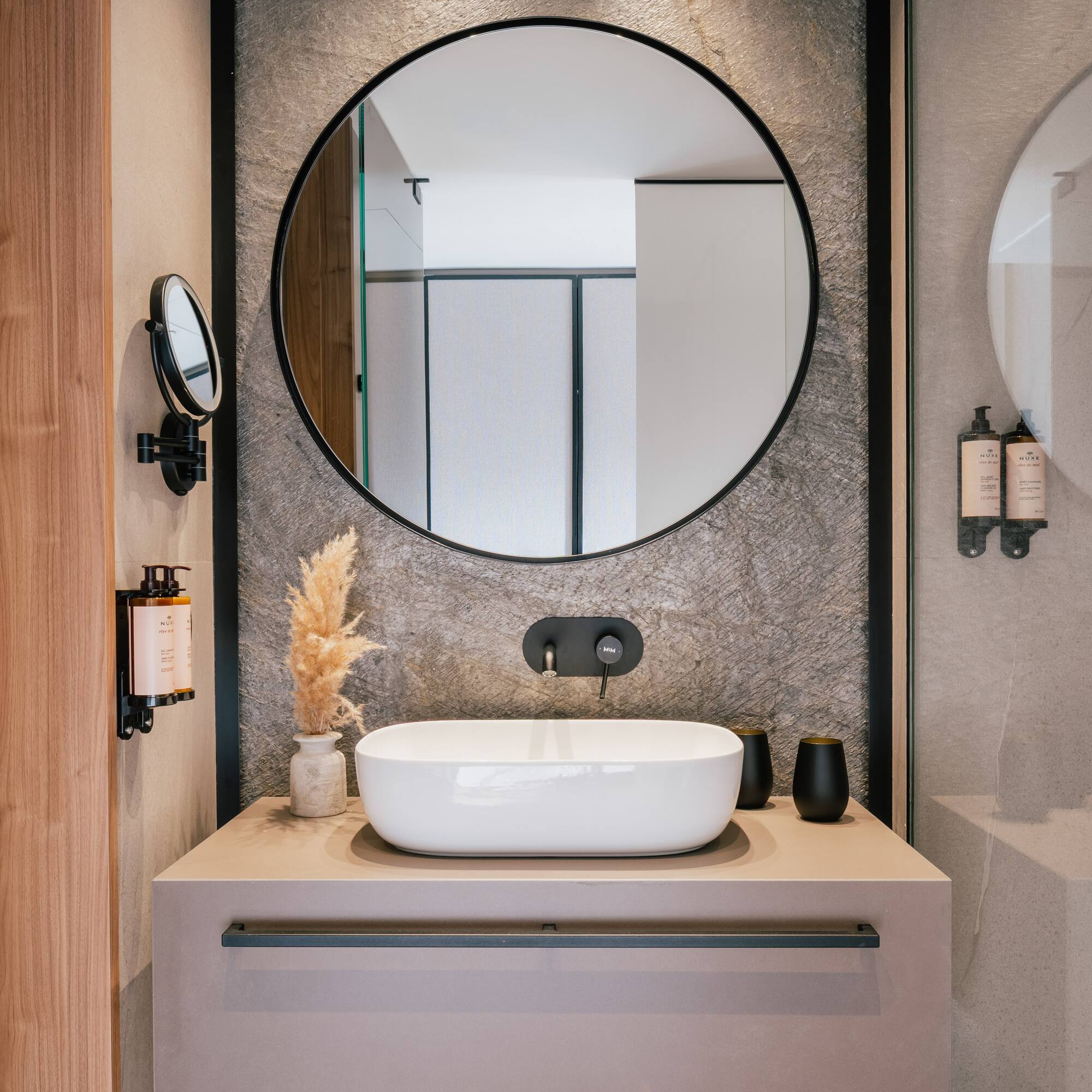 Sleek bathroom vanity, round mirror, white vessel sink, black faucet, stone wall.