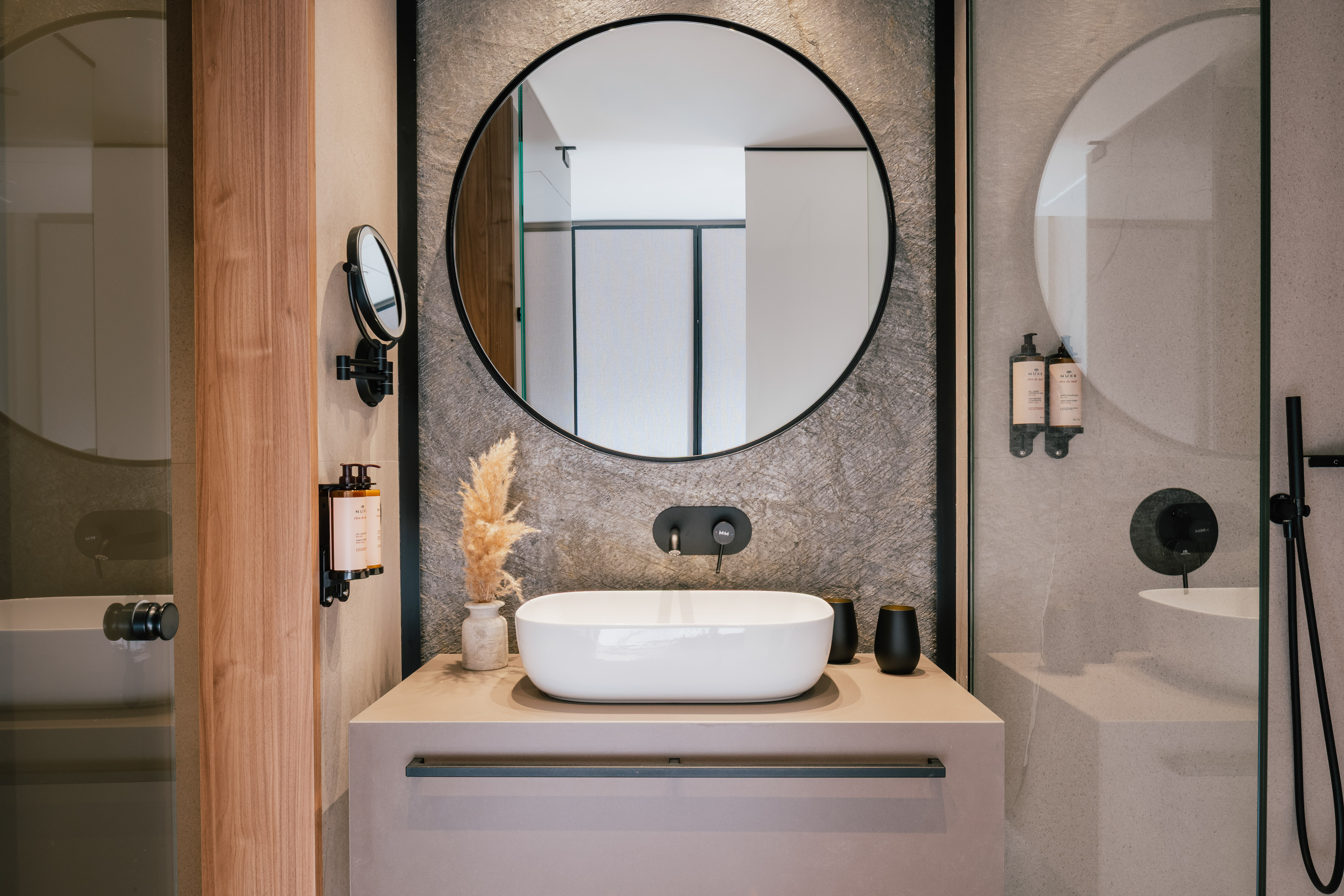 Sleek bathroom vanity, round mirror, white vessel sink, black faucet, stone wall.