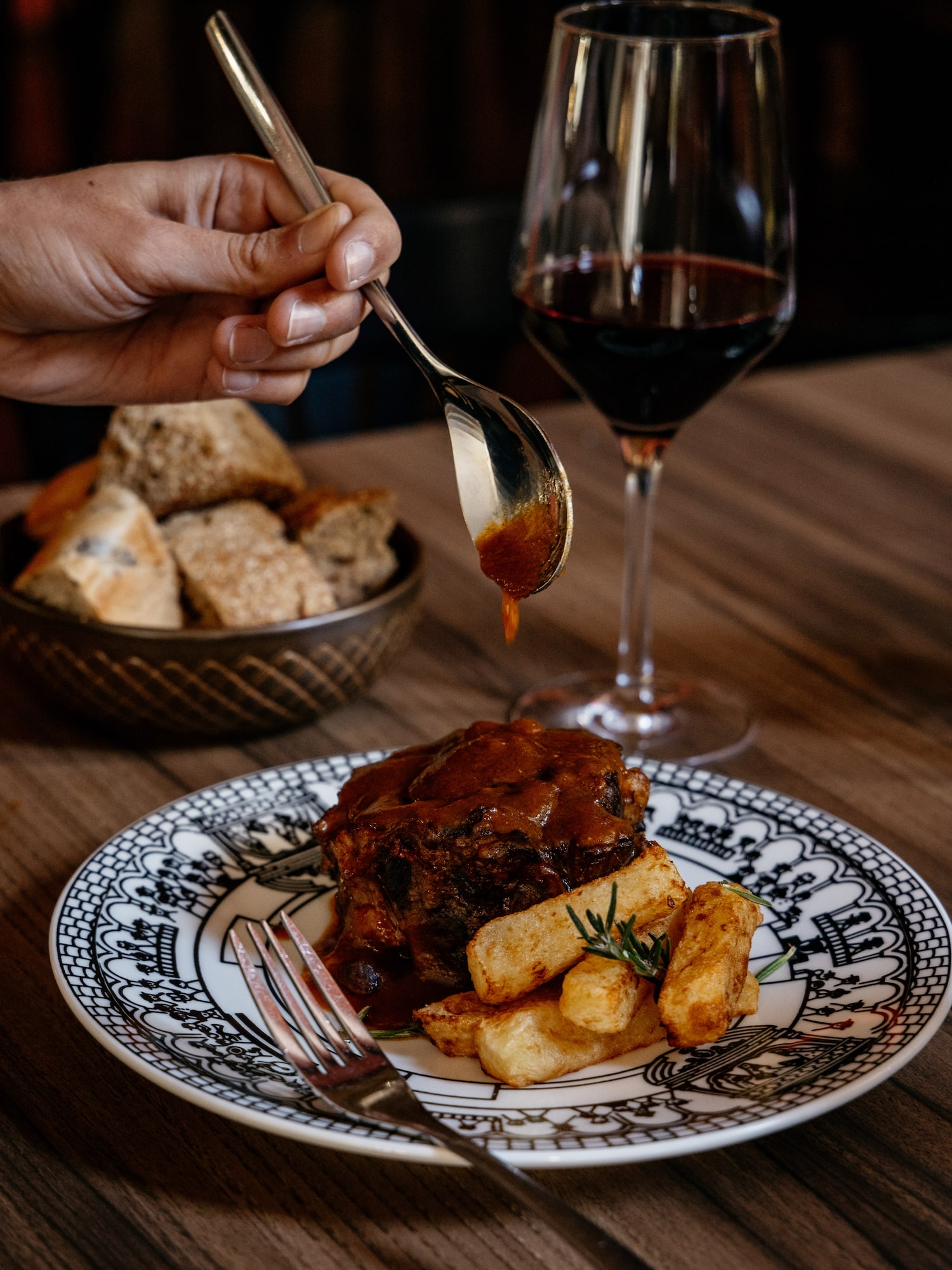 Mano sirviendo salsa a carne estofada, patatas con romero, vino tinto.