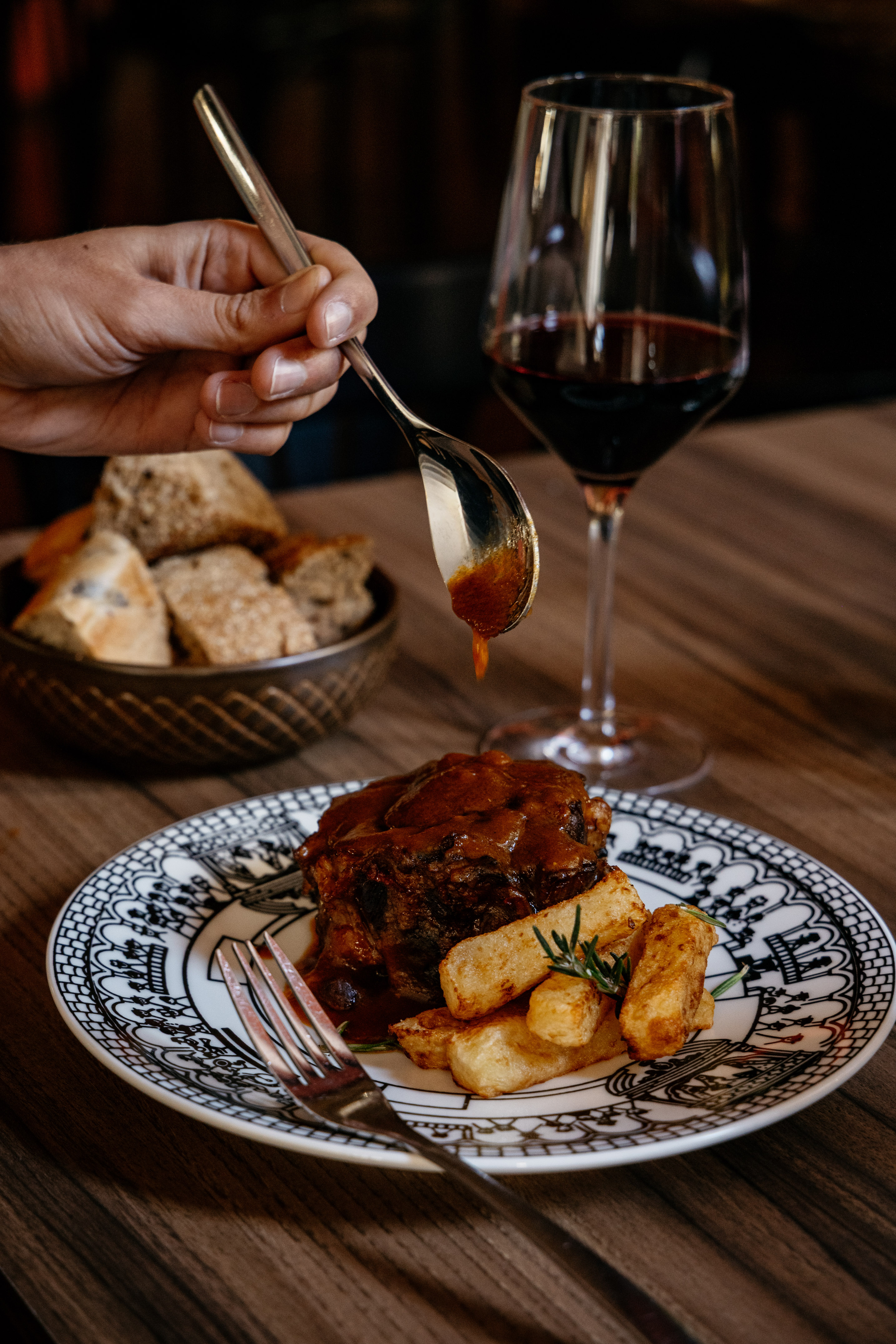 Mano sirviendo salsa a carne estofada, patatas con romero, vino tinto.