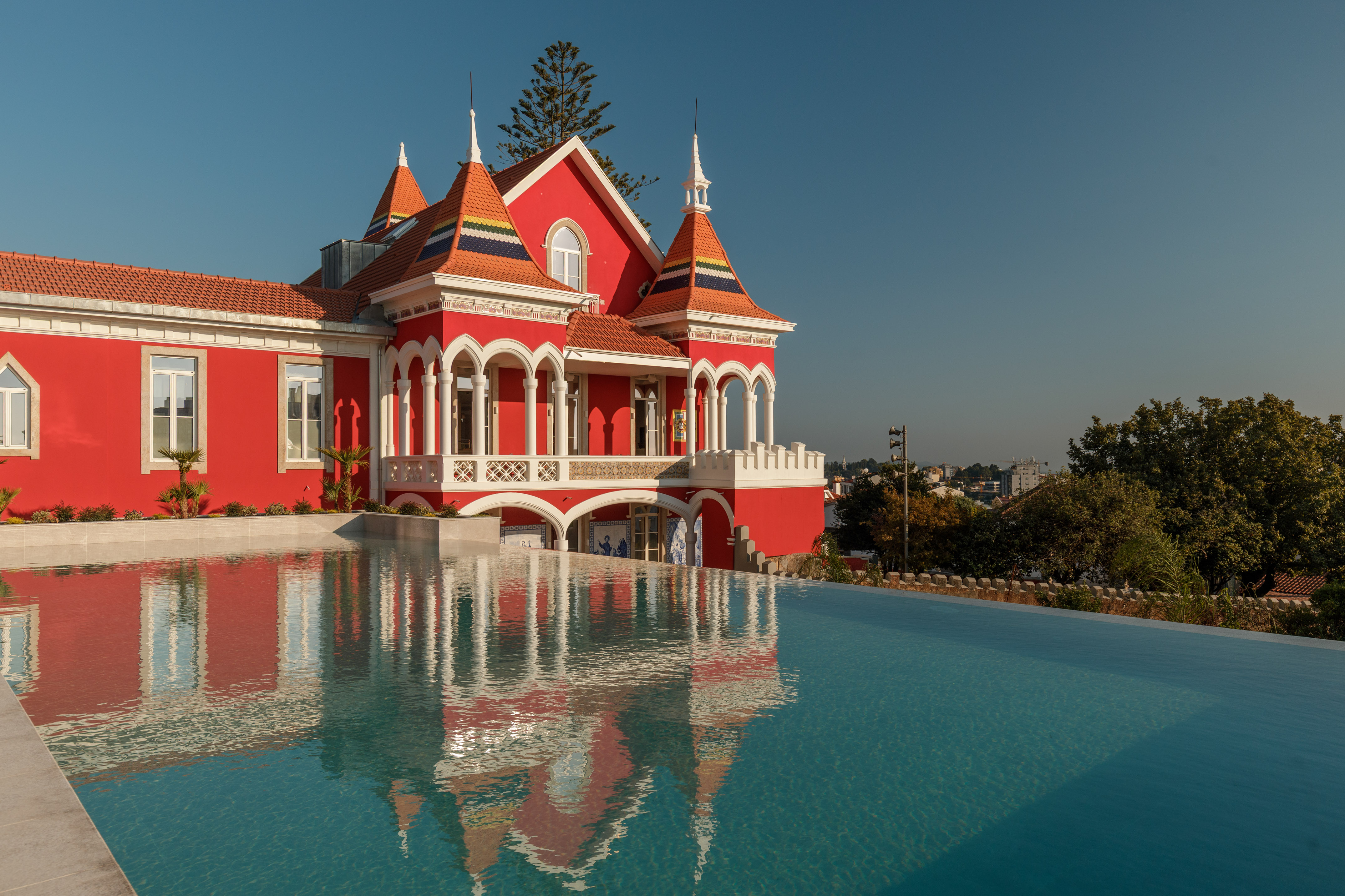 Red historic villa reflected in infinity pool under a clear blue sky.