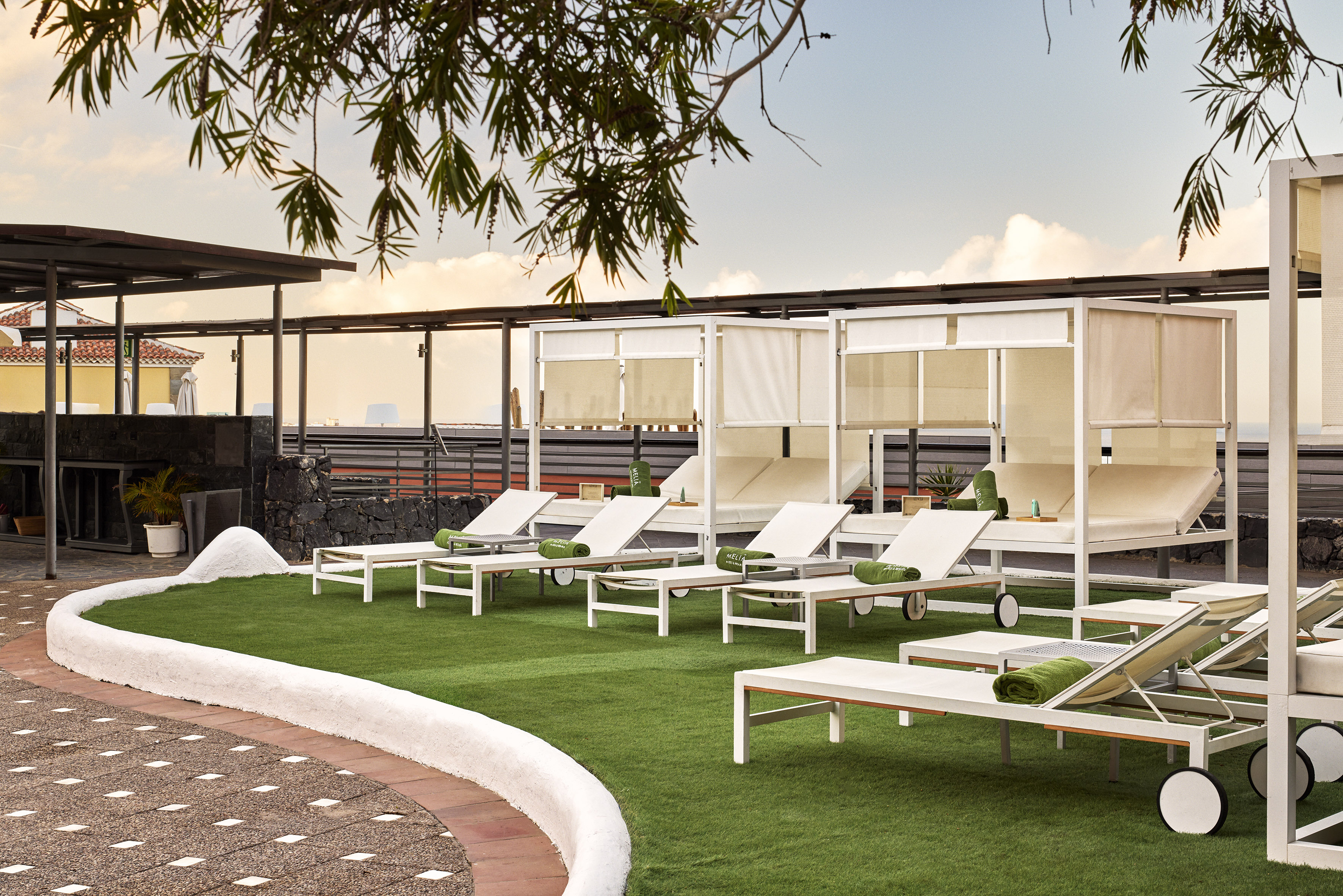 Resort outdoor lounge area with white sunbeds, cabanas, and green turf.