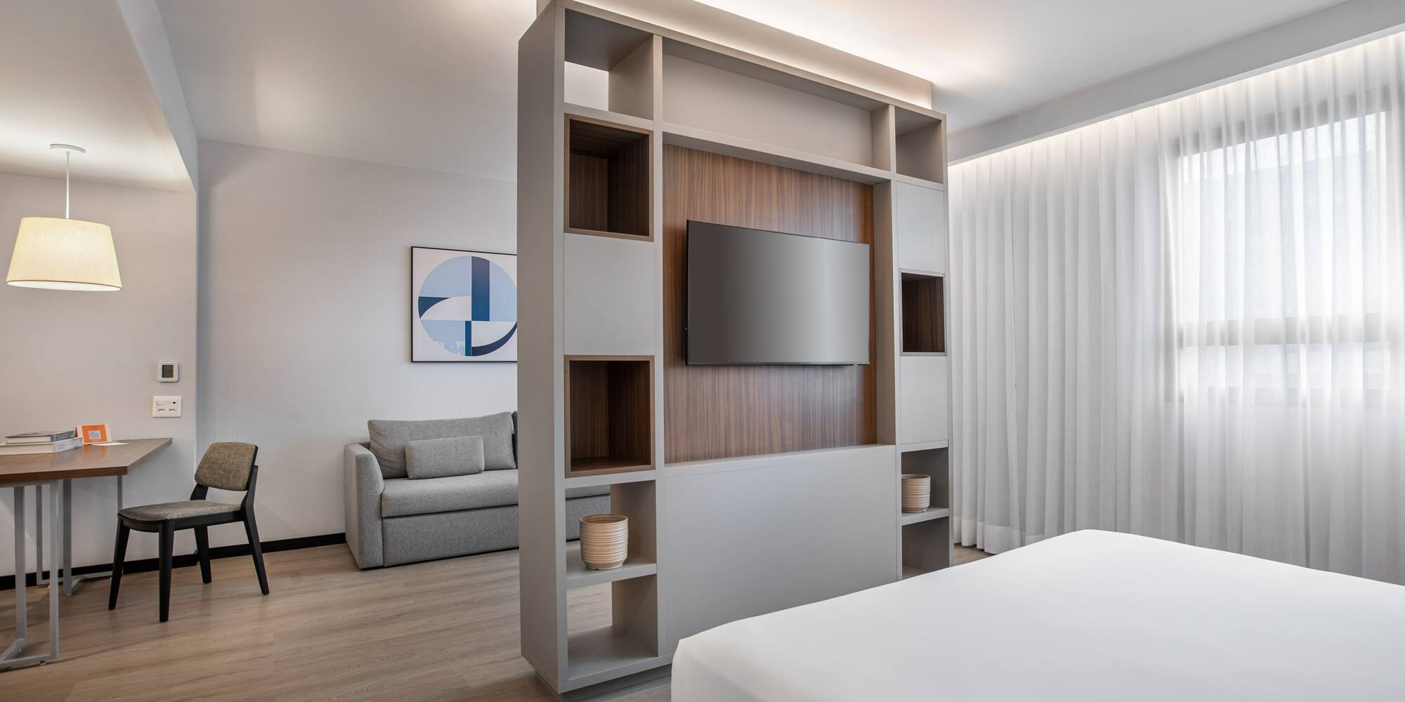 Modern hotel studio with living area, bed, TV, and neutral decor.