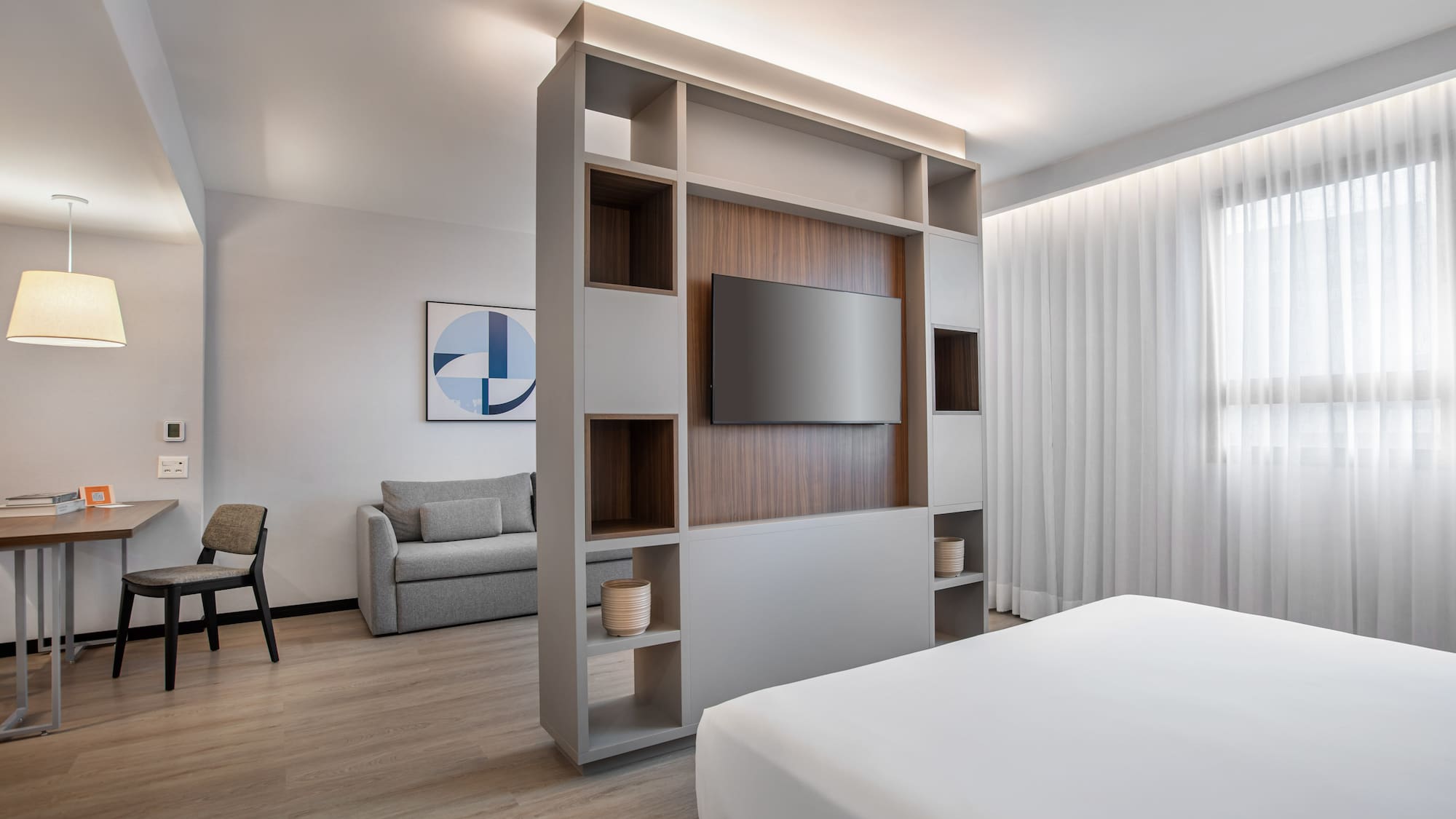 Modern hotel studio with living area, bed, TV, and neutral decor.