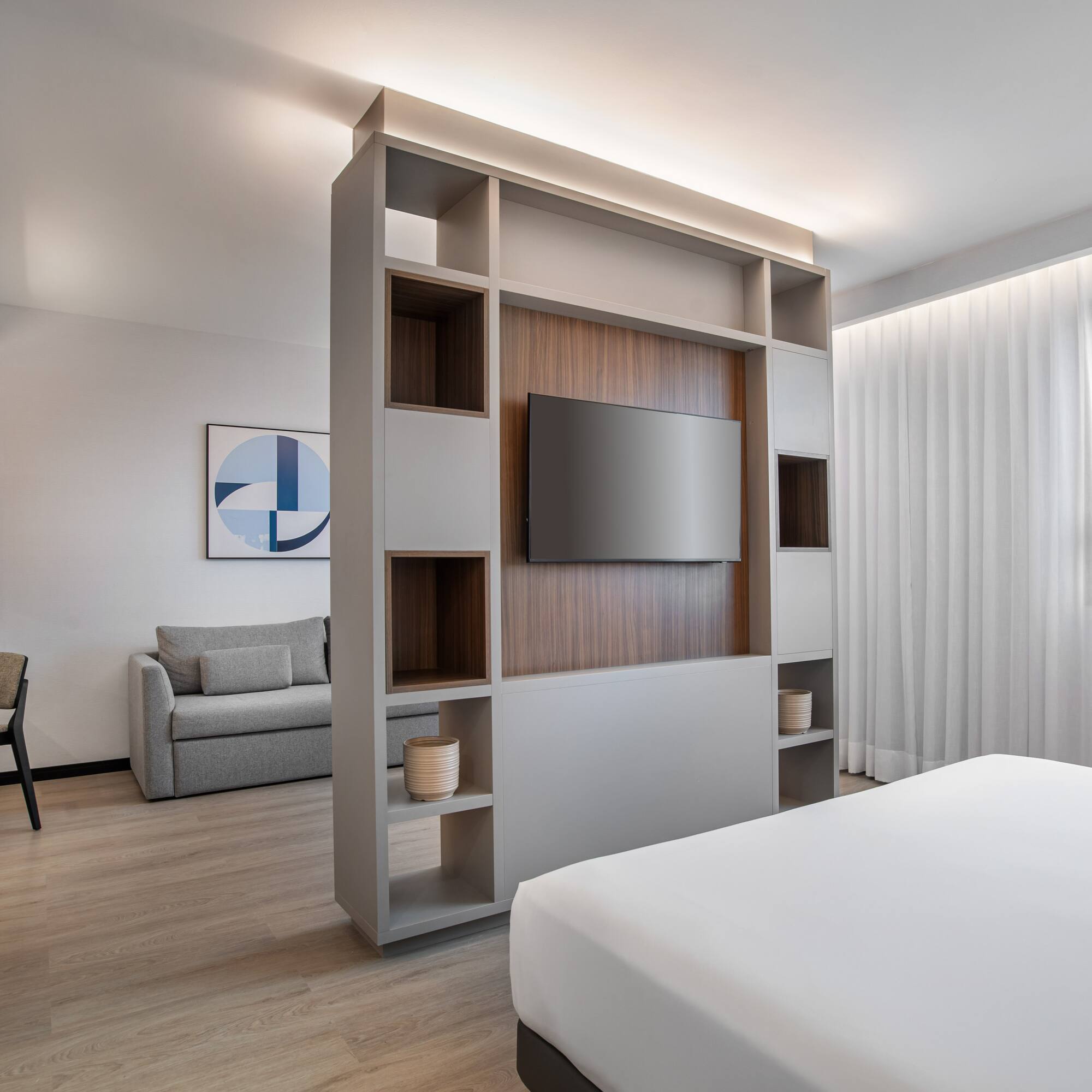Modern hotel studio with living area, bed, TV, and neutral decor.