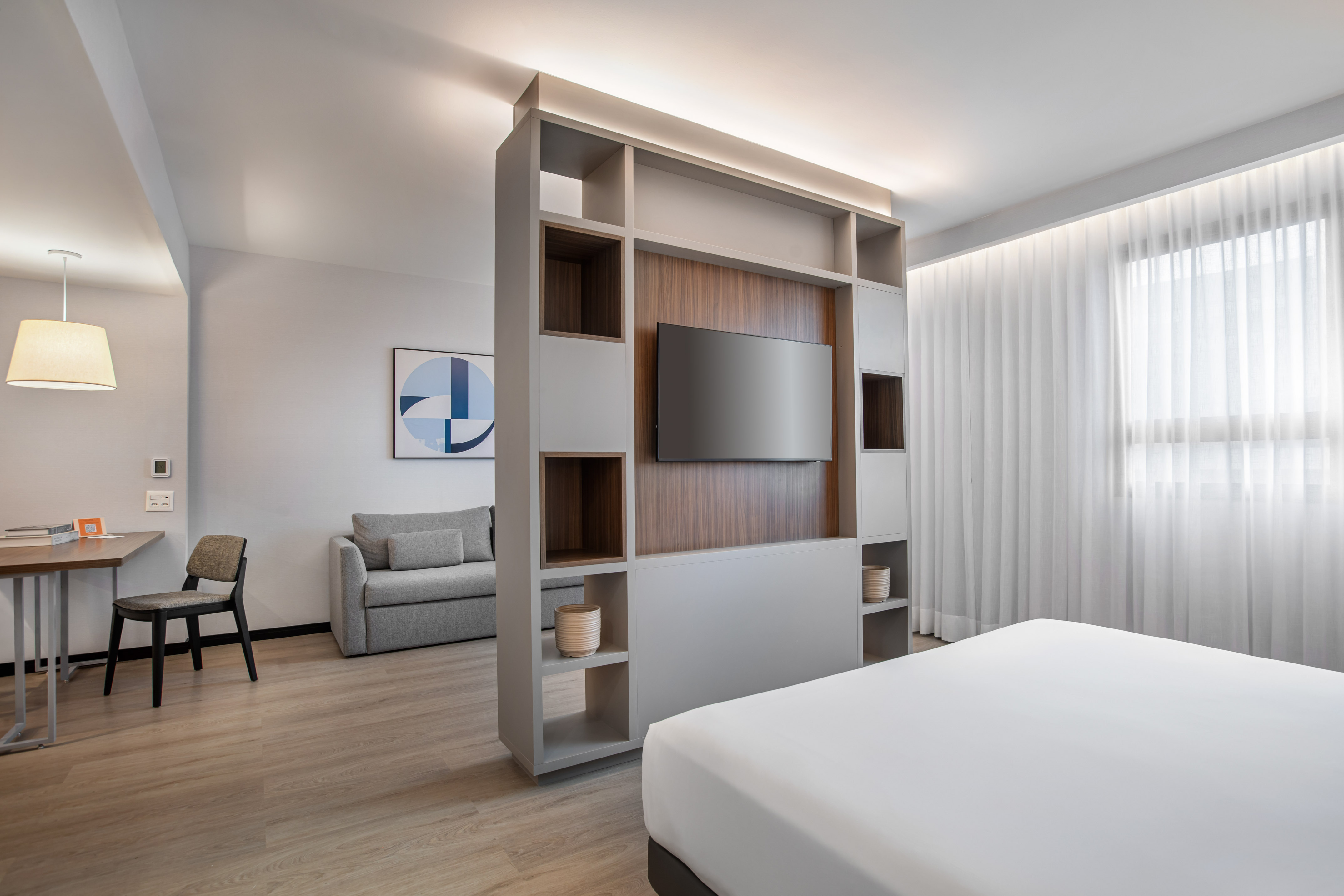 Modern hotel studio with living area, bed, TV, and neutral decor.