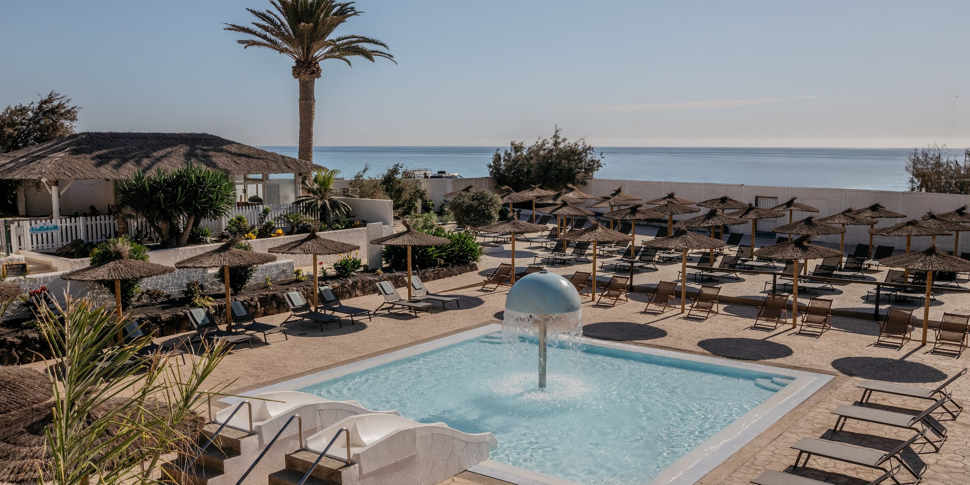 a pool with a fountain and umbrellas and a beach
