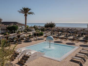 a pool with a fountain and umbrellas and a beach