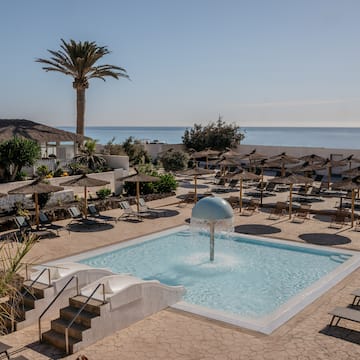 a pool with a fountain and umbrellas and a beach