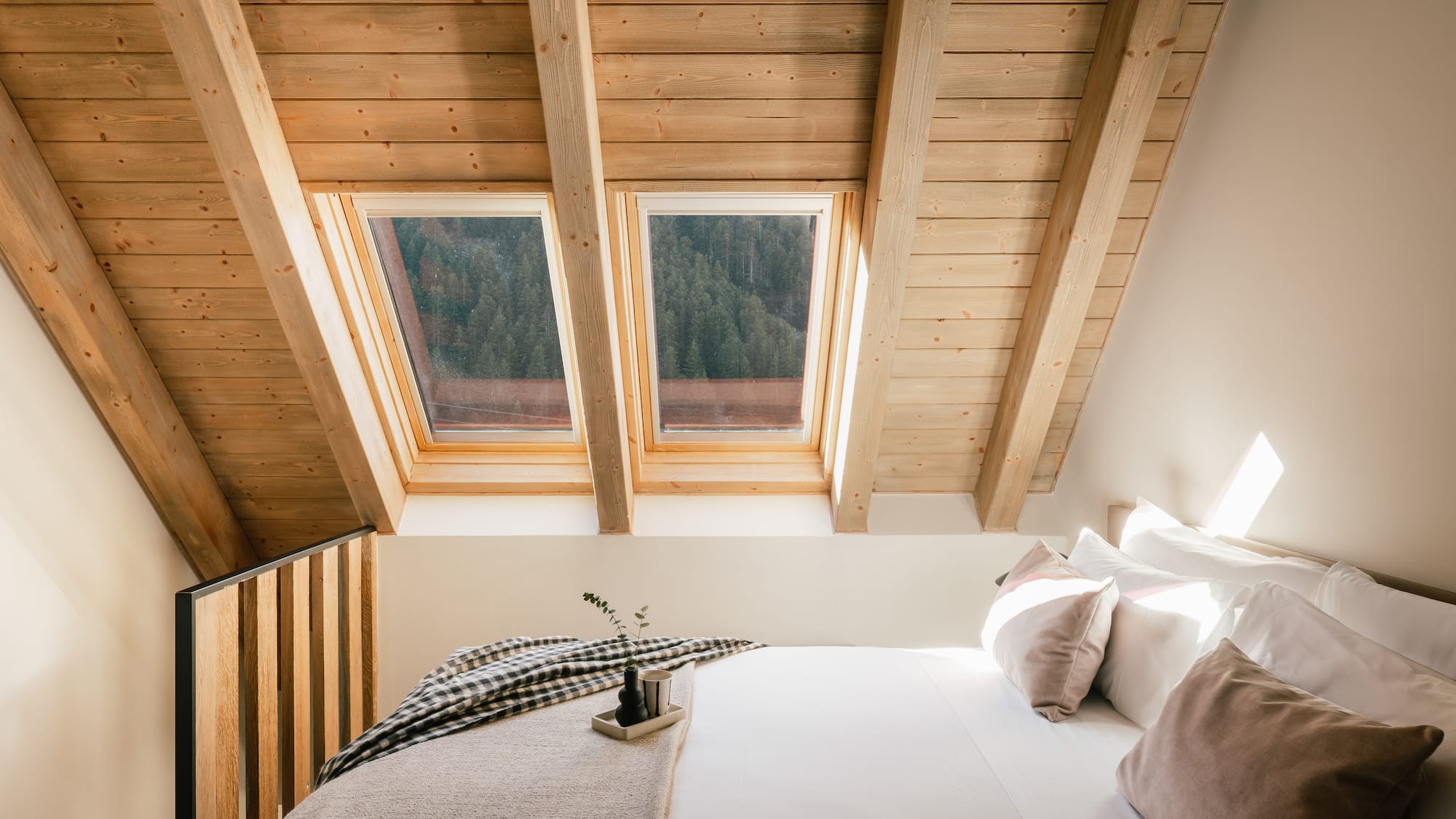 Cozy attic bedroom with wood ceiling, skylights, and forest view.