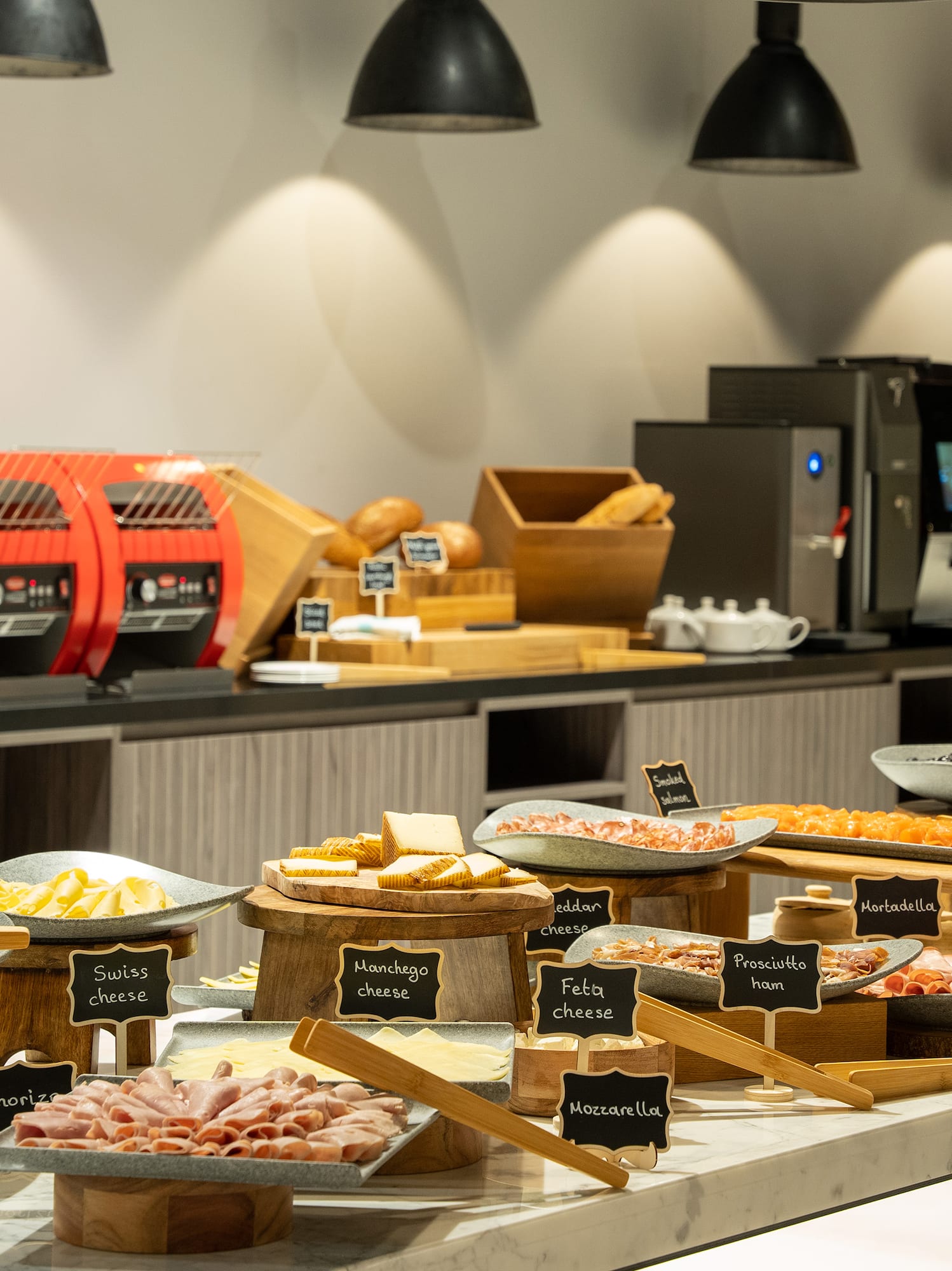 Breakfast buffet with various cold cuts, cheeses, bread, and coffee machines.