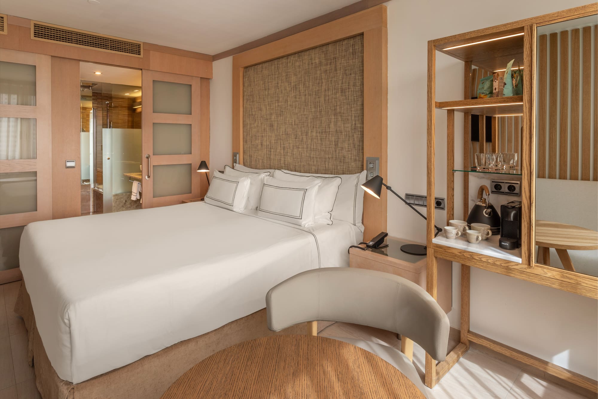 Modern hotel bedroom with king bed, wood accents, attached bath, and coffee maker.