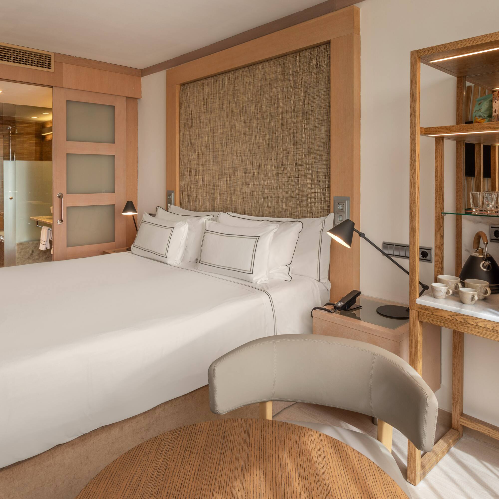 Modern hotel bedroom with king bed, wood accents, attached bath, and coffee maker.