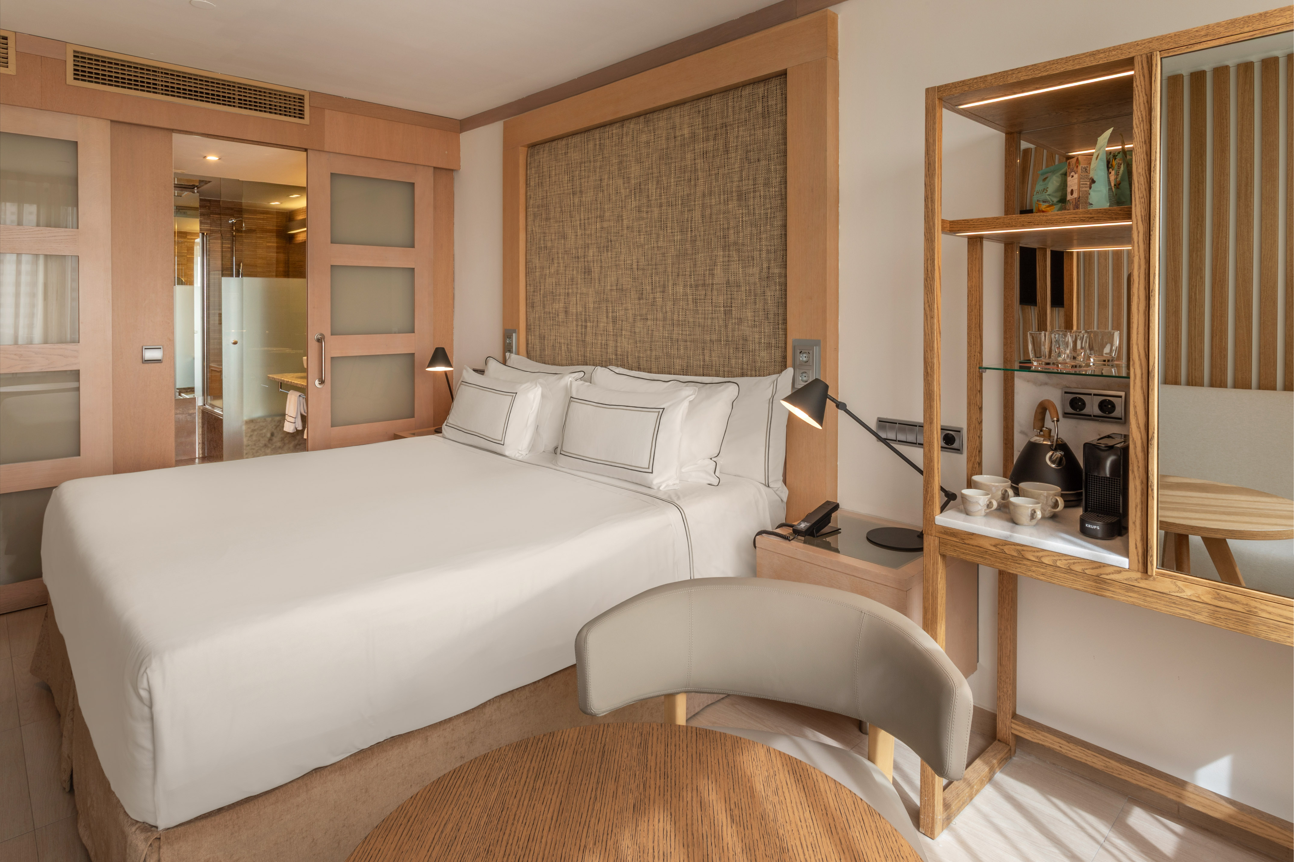 Modern hotel bedroom with king bed, wood accents, attached bath, and coffee maker.