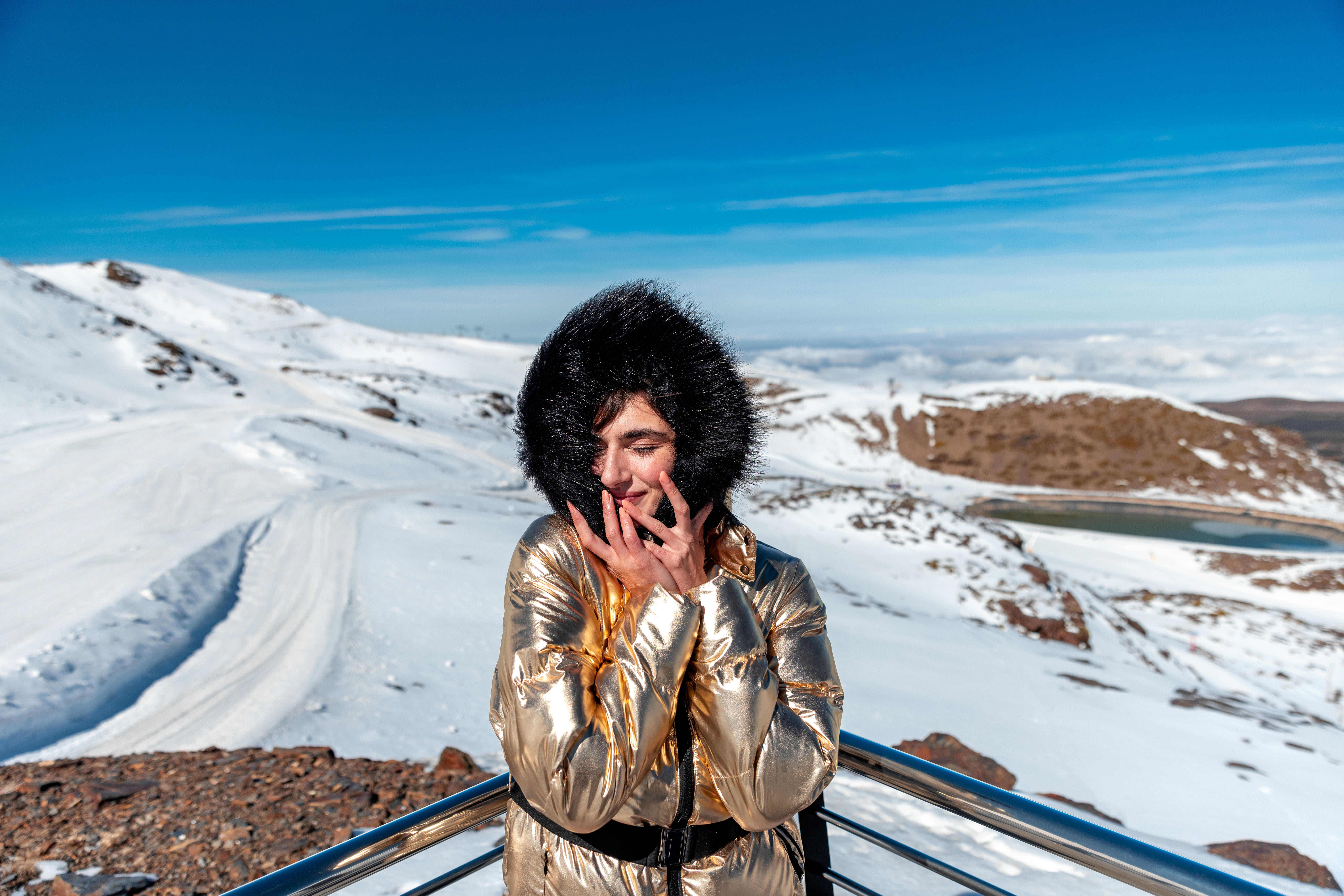 a woman in a gold coat with a fur hood on a snowy mountain