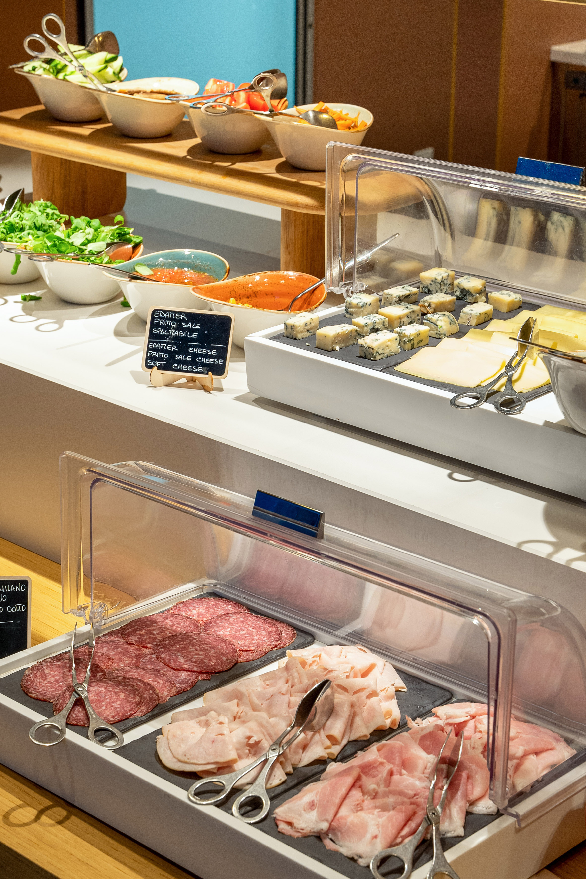 Buffet with sliced salami, ham, various cheeses, and fresh salads.