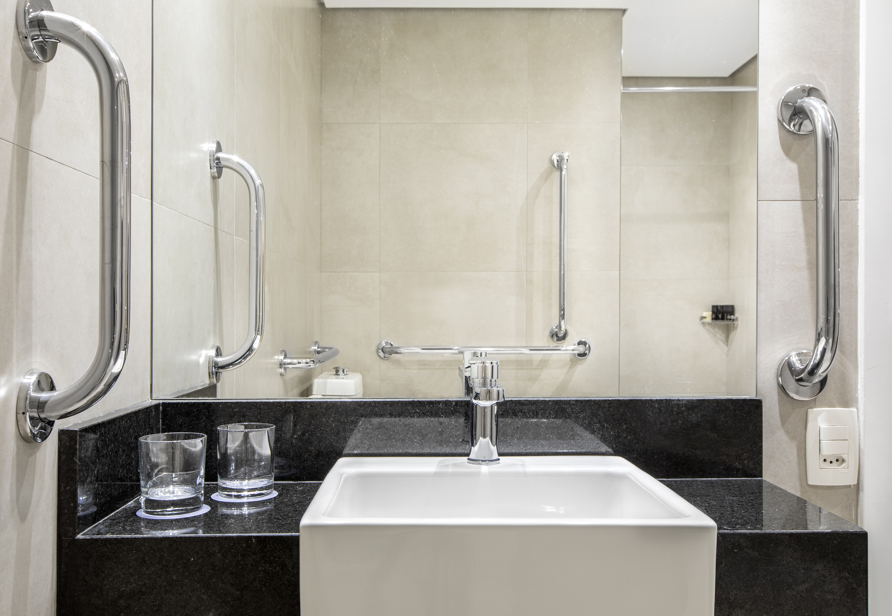 ADA compliant bathroom vanity with white sink, black counter, mirror, grab bars.
