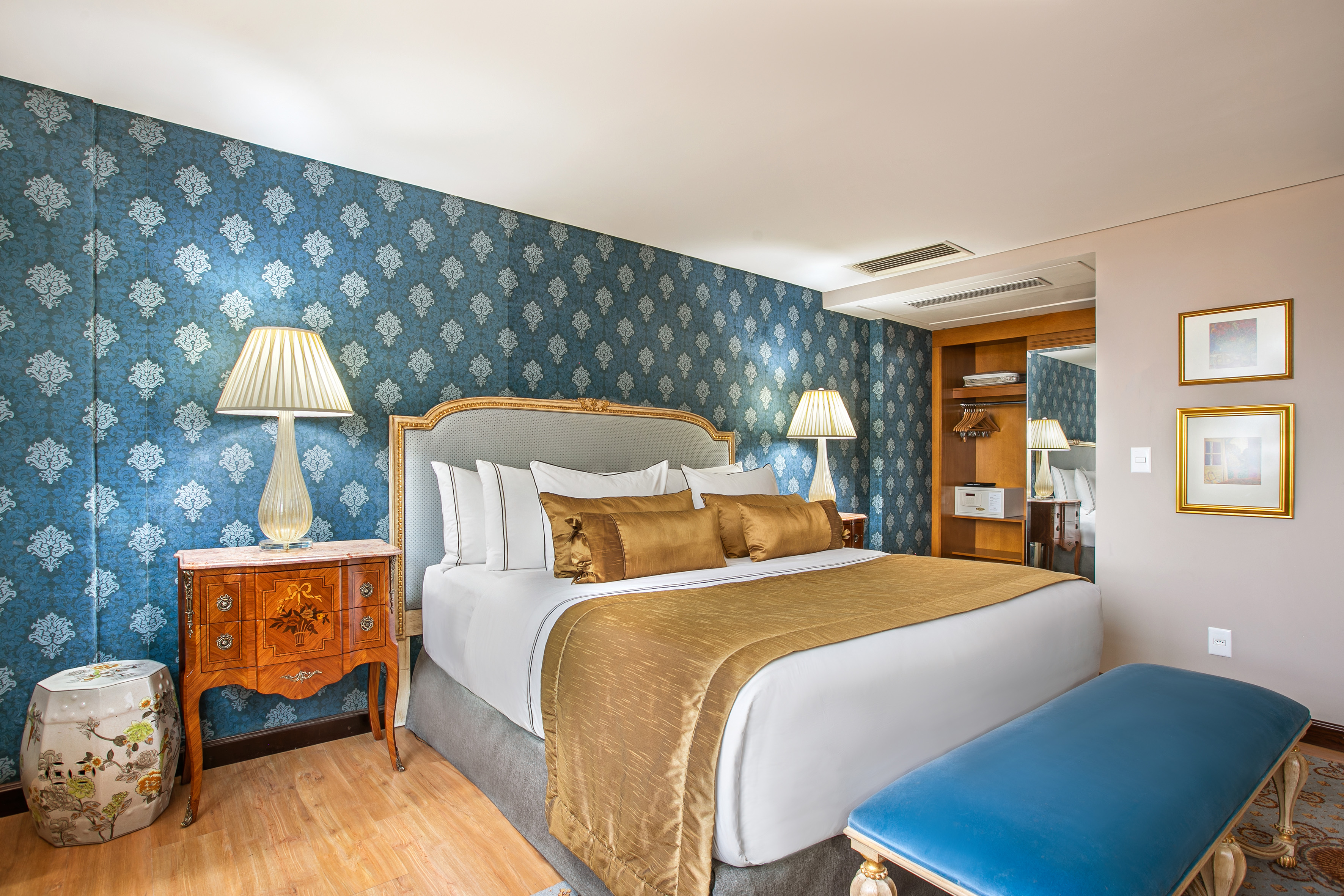 Luxury hotel room with king bed, blue damask wallpaper, and gold accents.