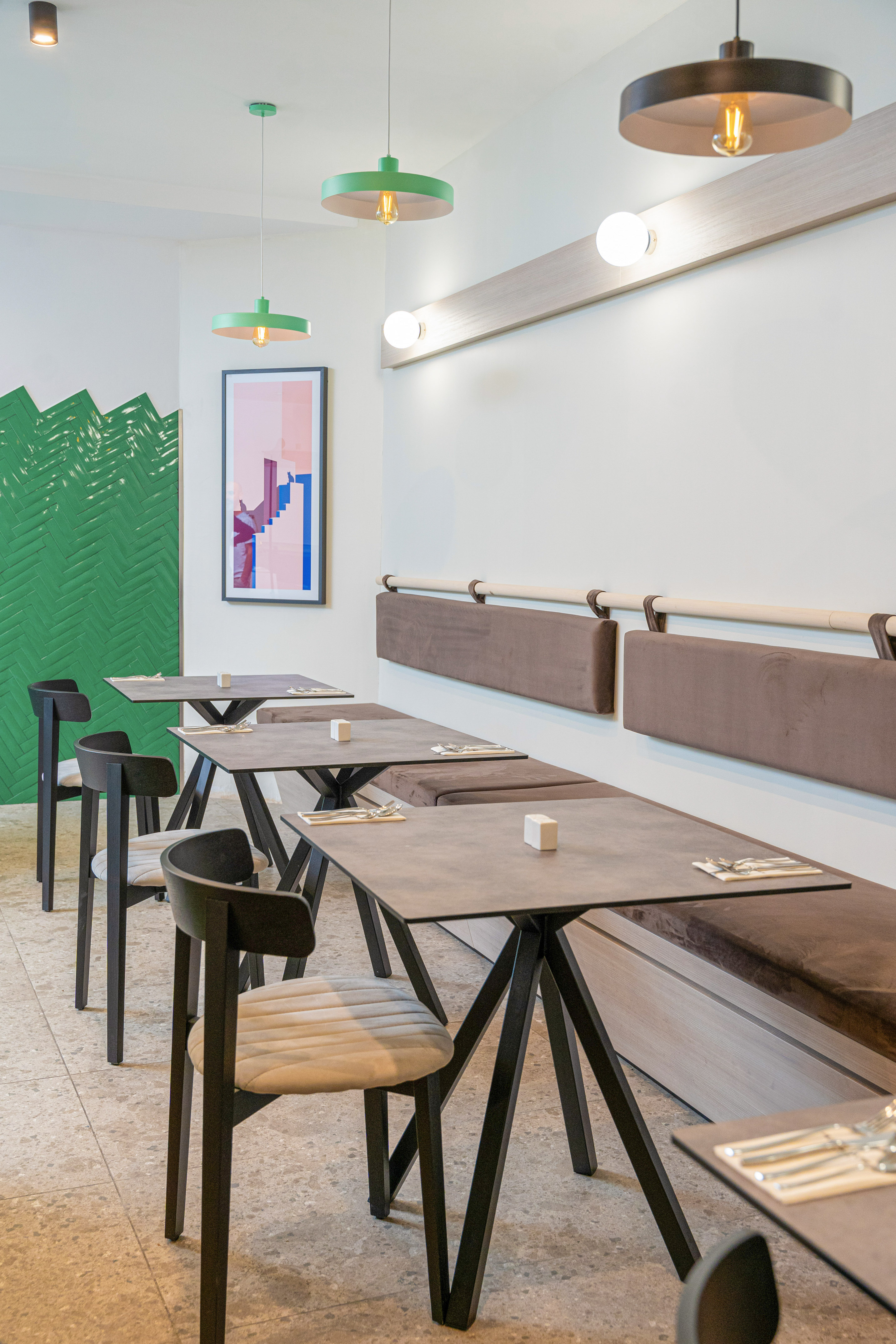 Modern restaurant interior, grey tables, brown banquettes, green tiled wall.