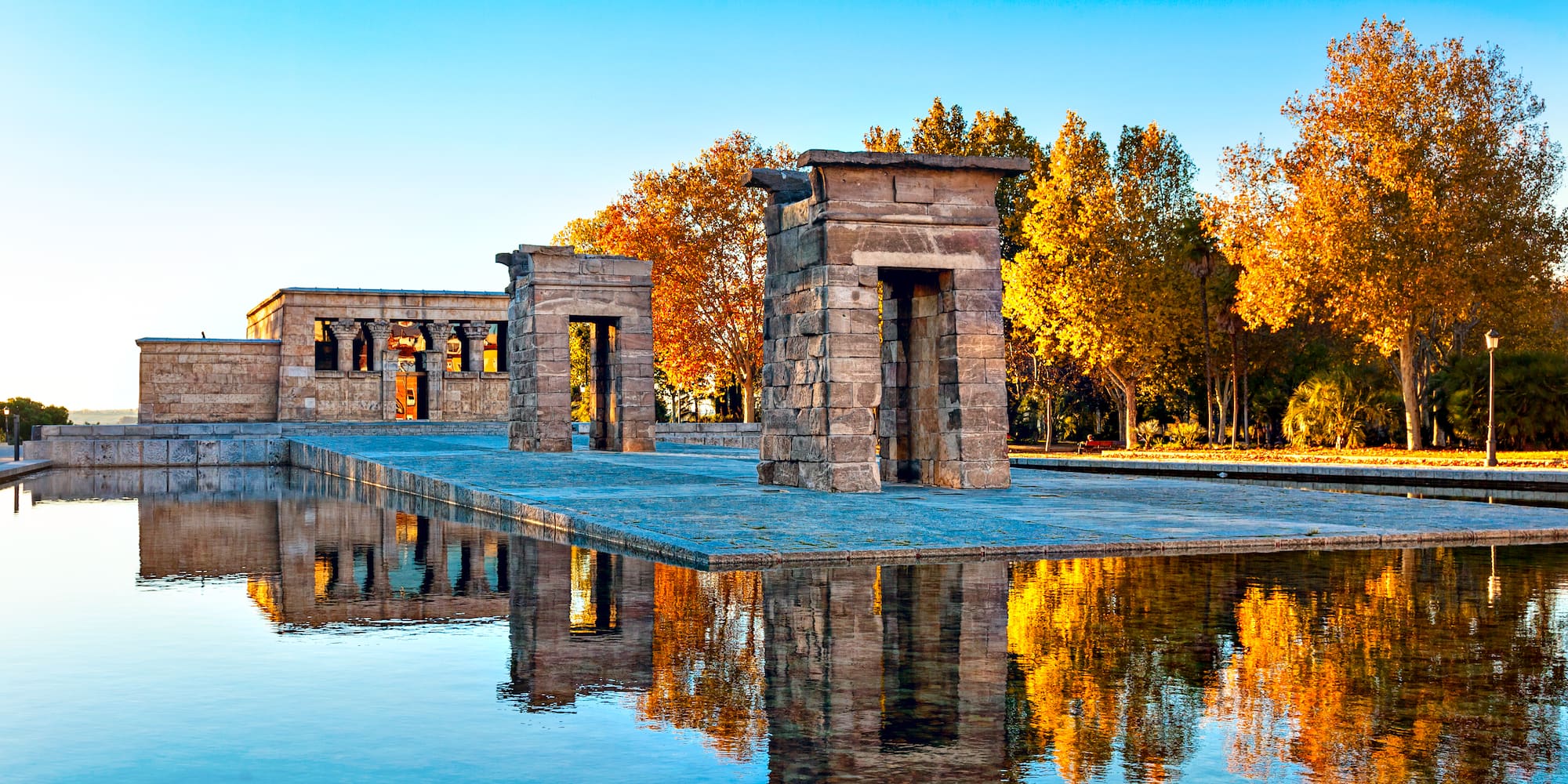 Temple of Debod, Madrid: stone temple reflected in water, vibrant autumn trees.