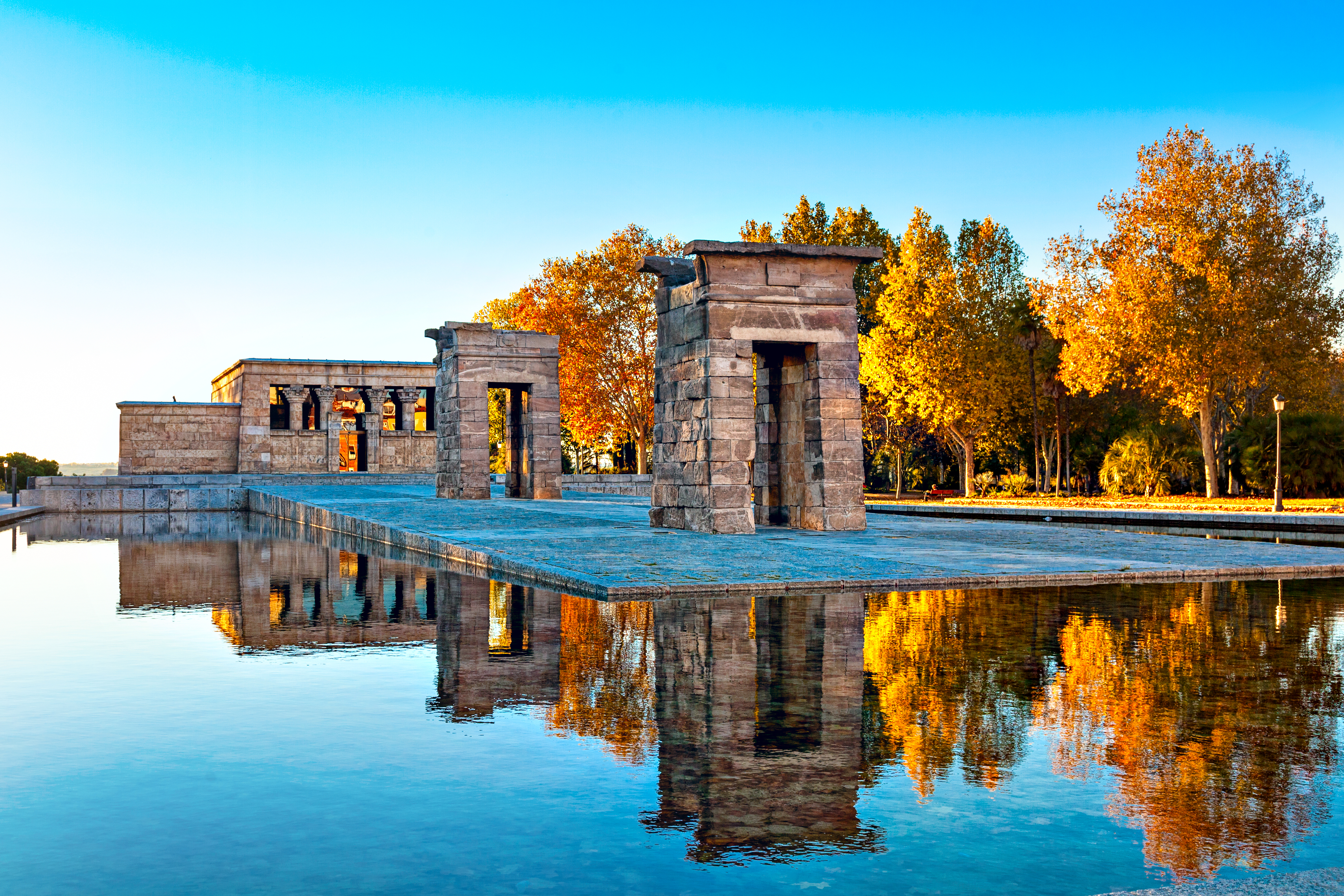 Temple of Debod, Madrid: stone temple reflected in water, vibrant autumn trees.