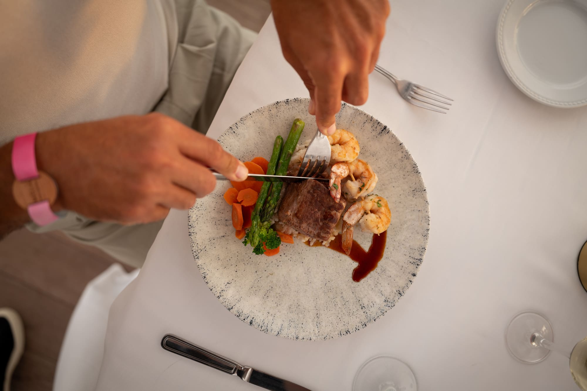 Manos cortando bistec y camarones con vegetales en cena gourmet.