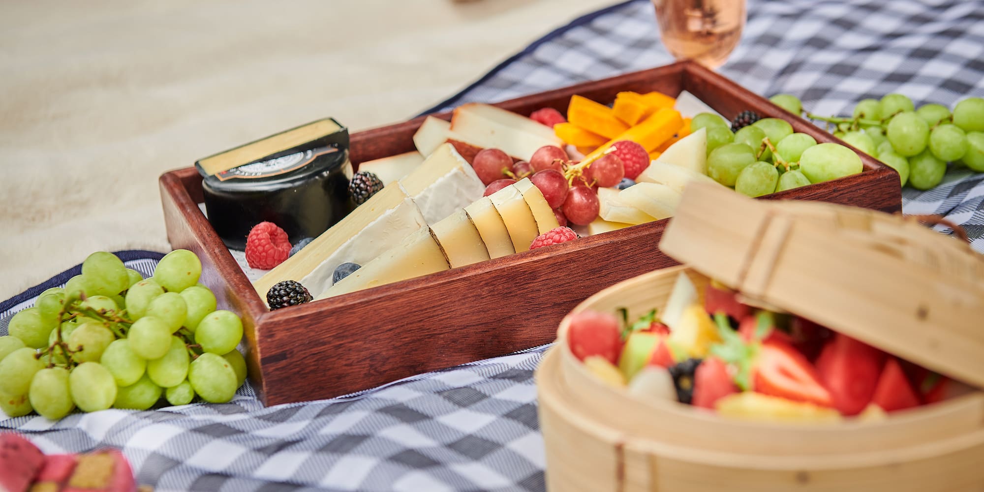 a tray of fruit and cheese on a blanket