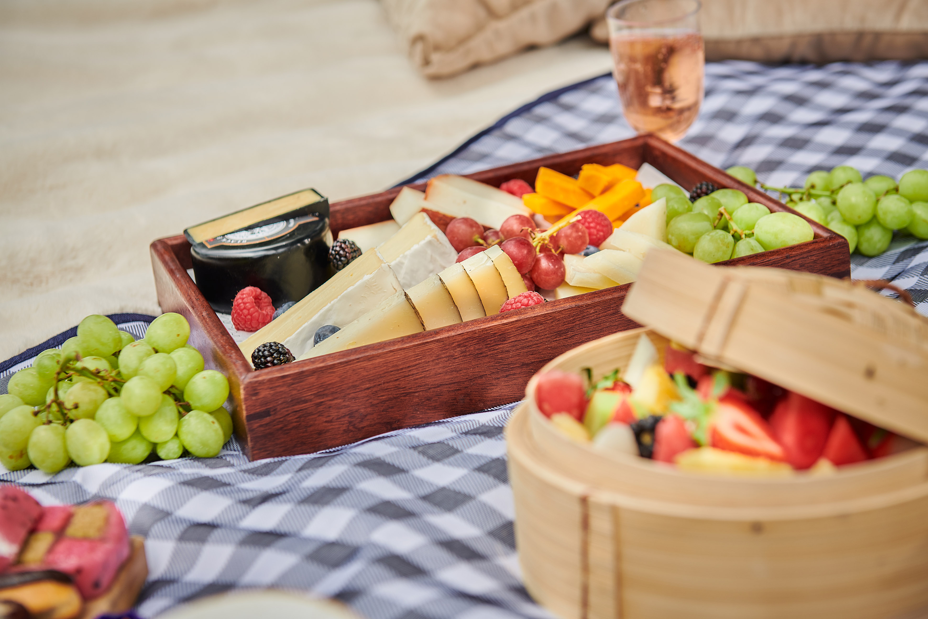 Picnic cheese and fruit platter with grapes, berries, and wine.