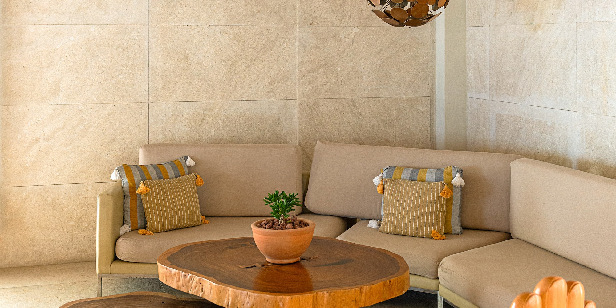 Lounge with live edge tables, beige sofa, wooden hand chair, and pendant lights.