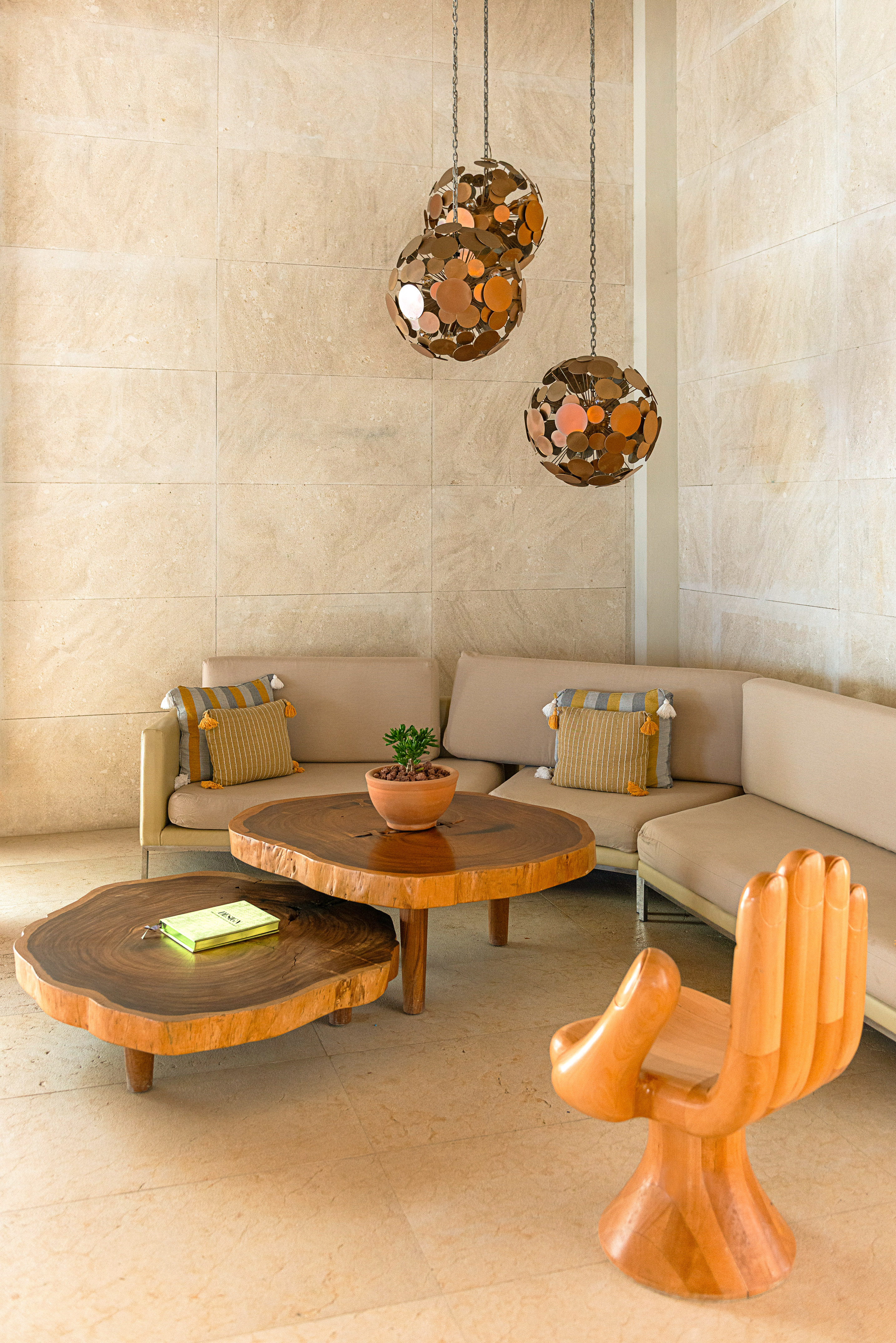 Lounge with live edge tables, beige sofa, wooden hand chair, and pendant lights.