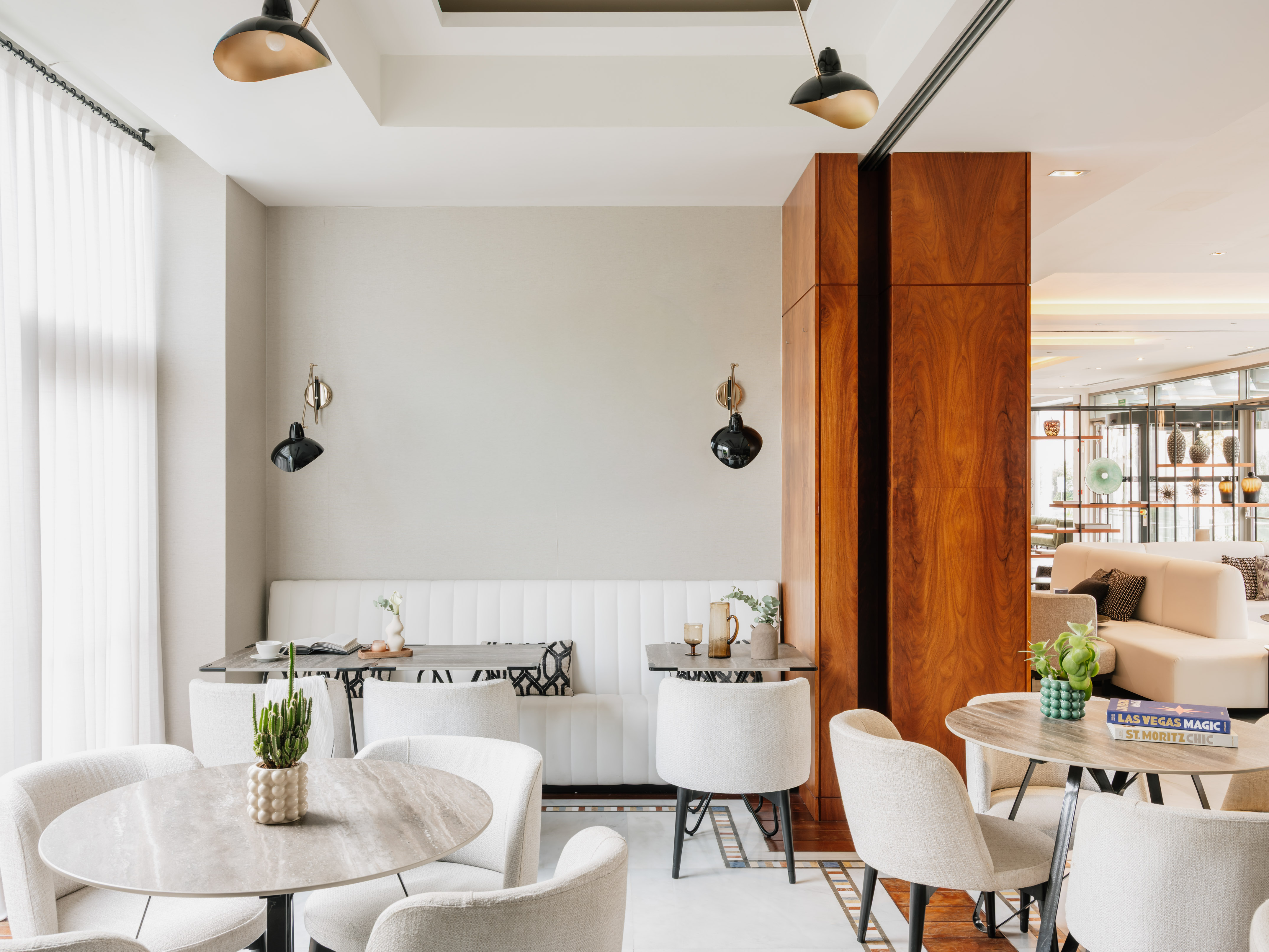 Modern hotel lounge with white seating, marble tables, and warm wooden accents.
