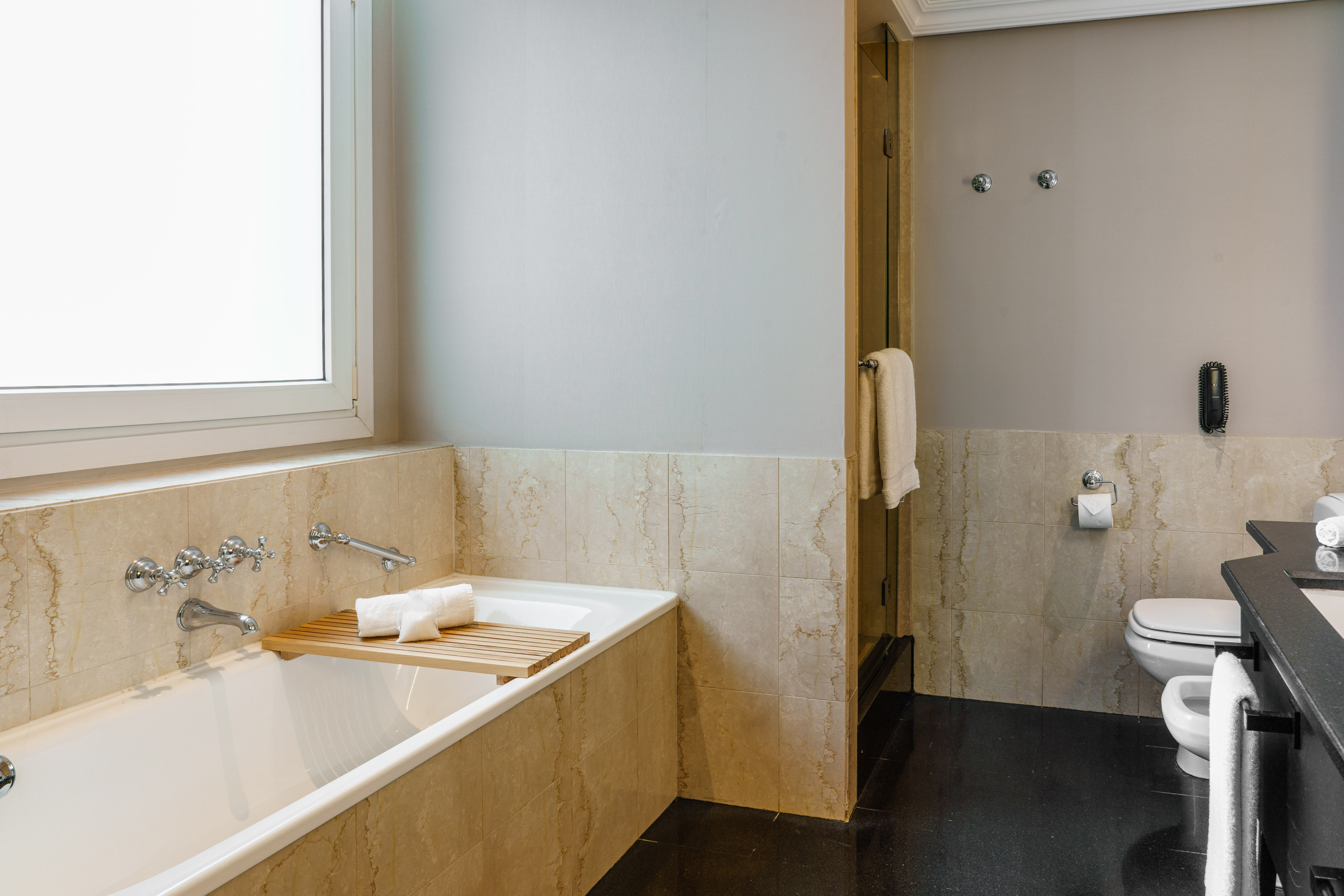 Modern bathroom with bathtub, window, marble walls, toilet, and dark floor.
