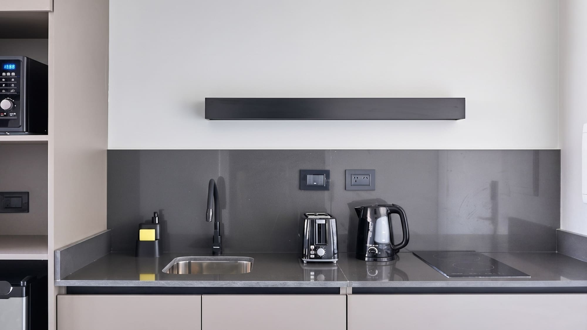 Modern grey kitchenette with beige cabinets, sink, and black appliances.
