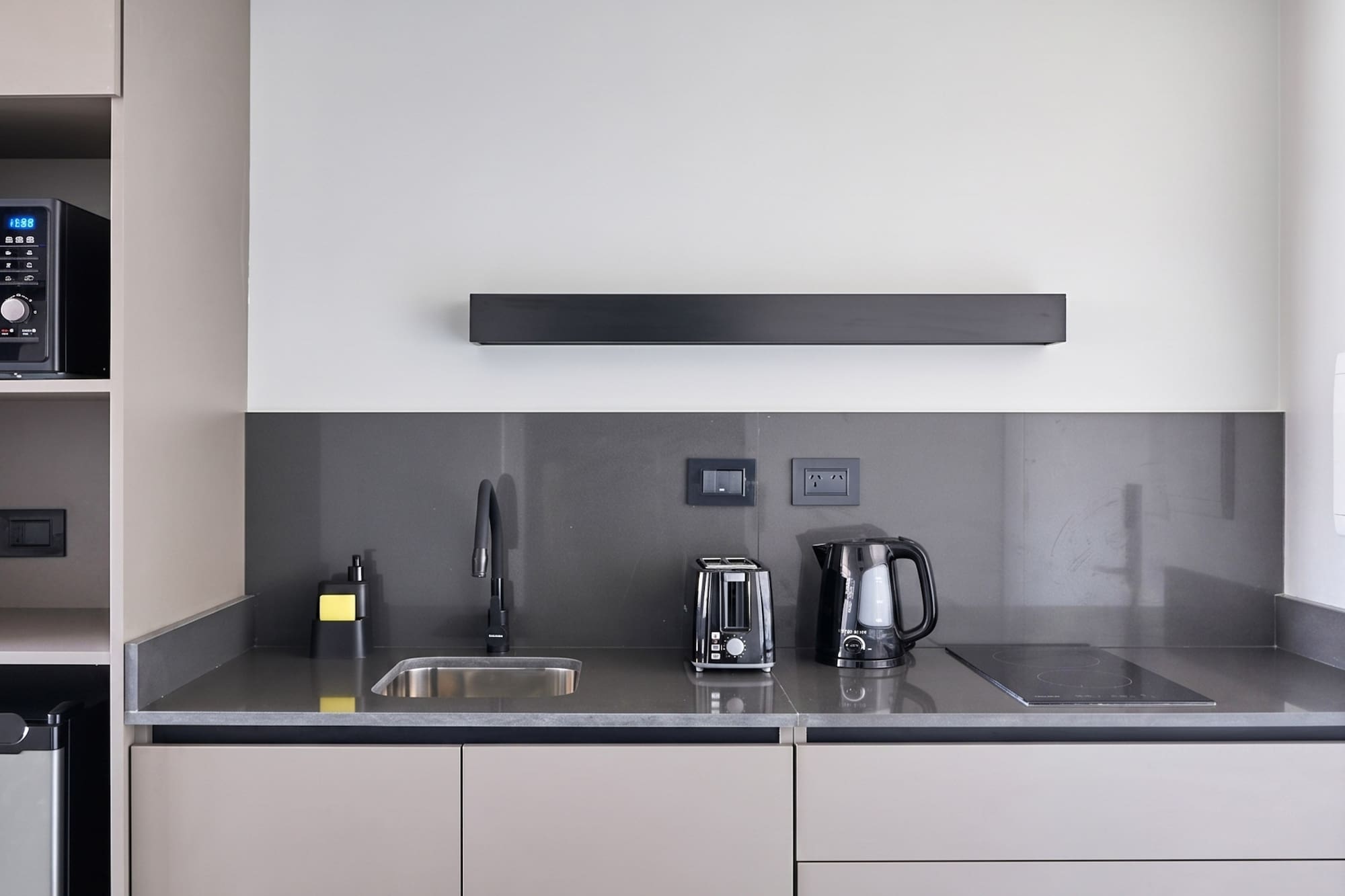 Modern kitchenette with grey cabinets, dark countertop, sink, toaster, and kettle.