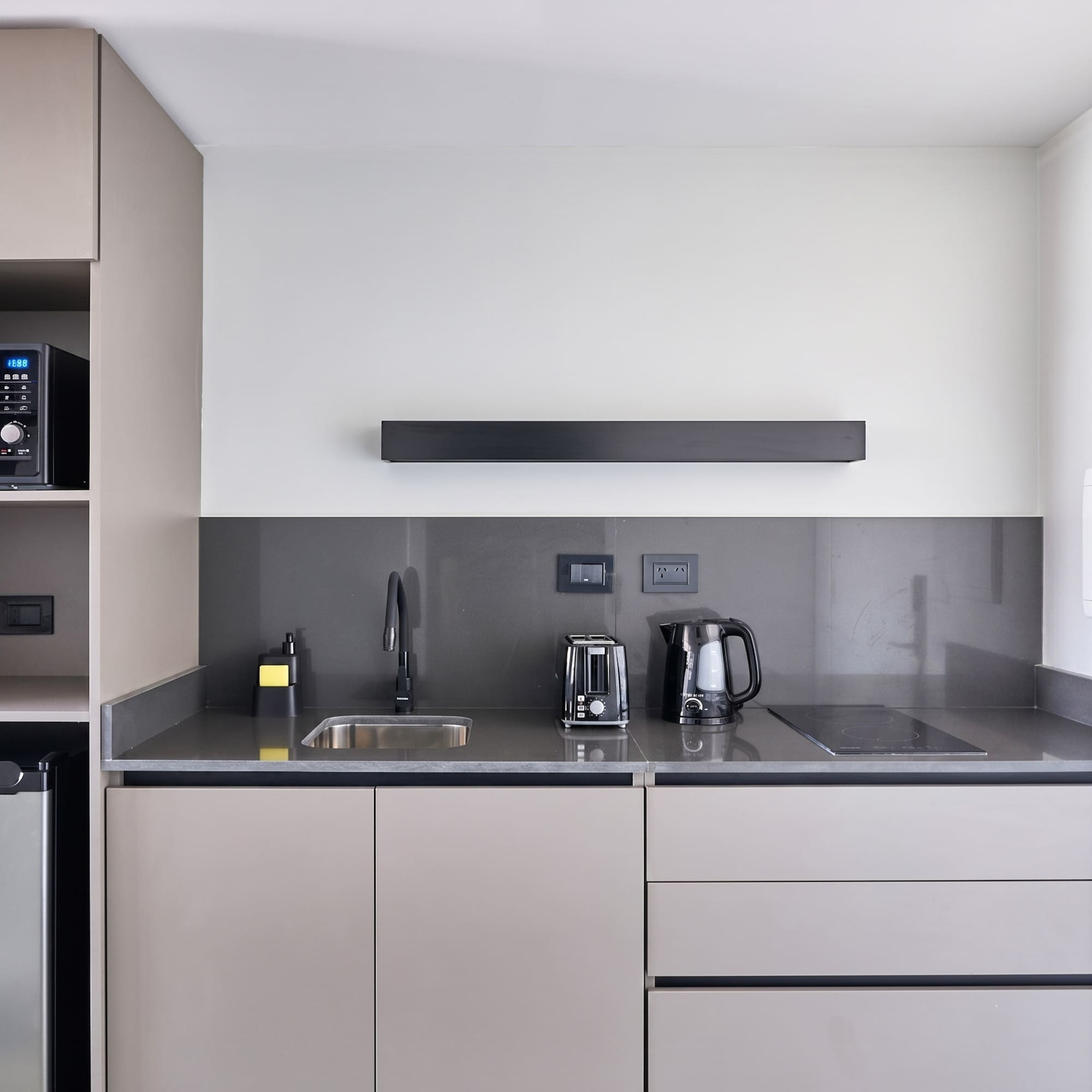 Modern kitchenette with grey cabinets, dark countertop, sink, toaster, and kettle.