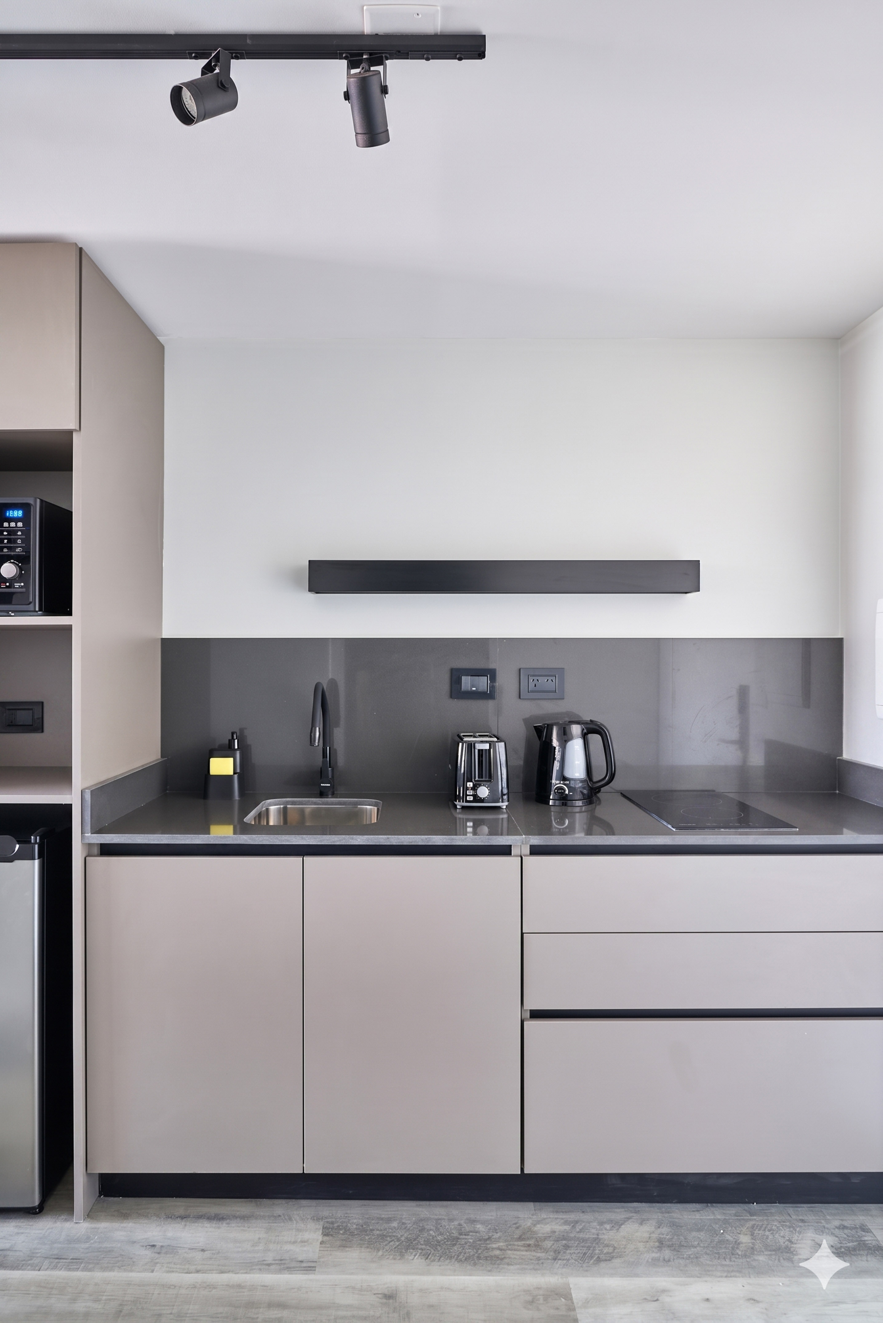 Modern grey kitchenette with beige cabinets, sink, and black appliances.