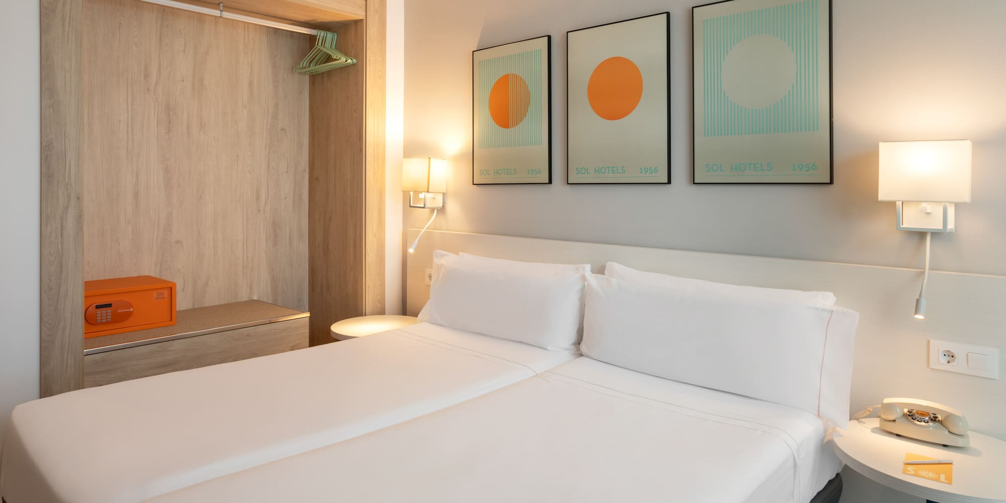 Modern hotel bedroom with twin beds, safe, and Sol Hotels artwork.