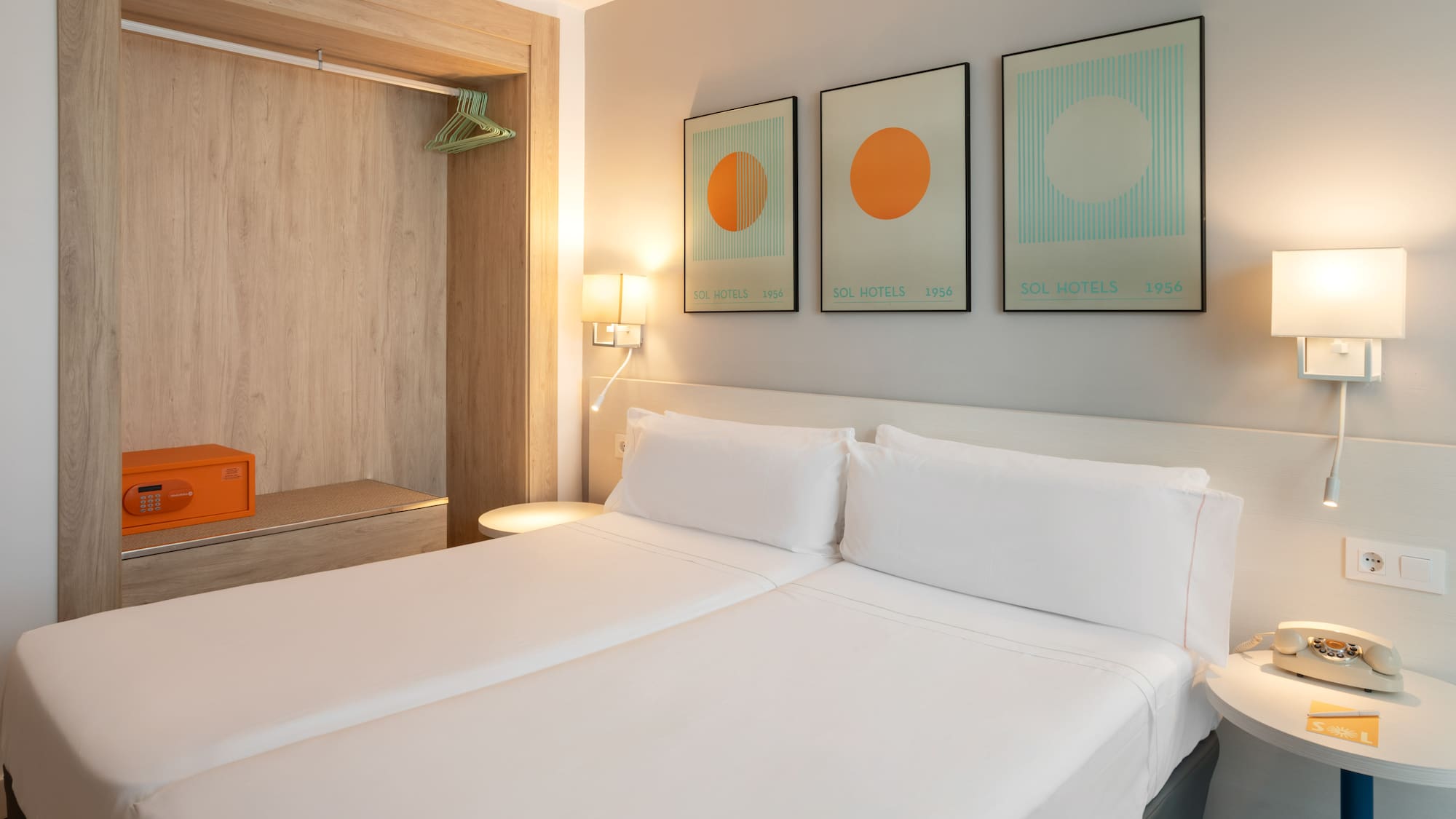 Modern hotel bedroom with twin beds, safe, and Sol Hotels artwork.