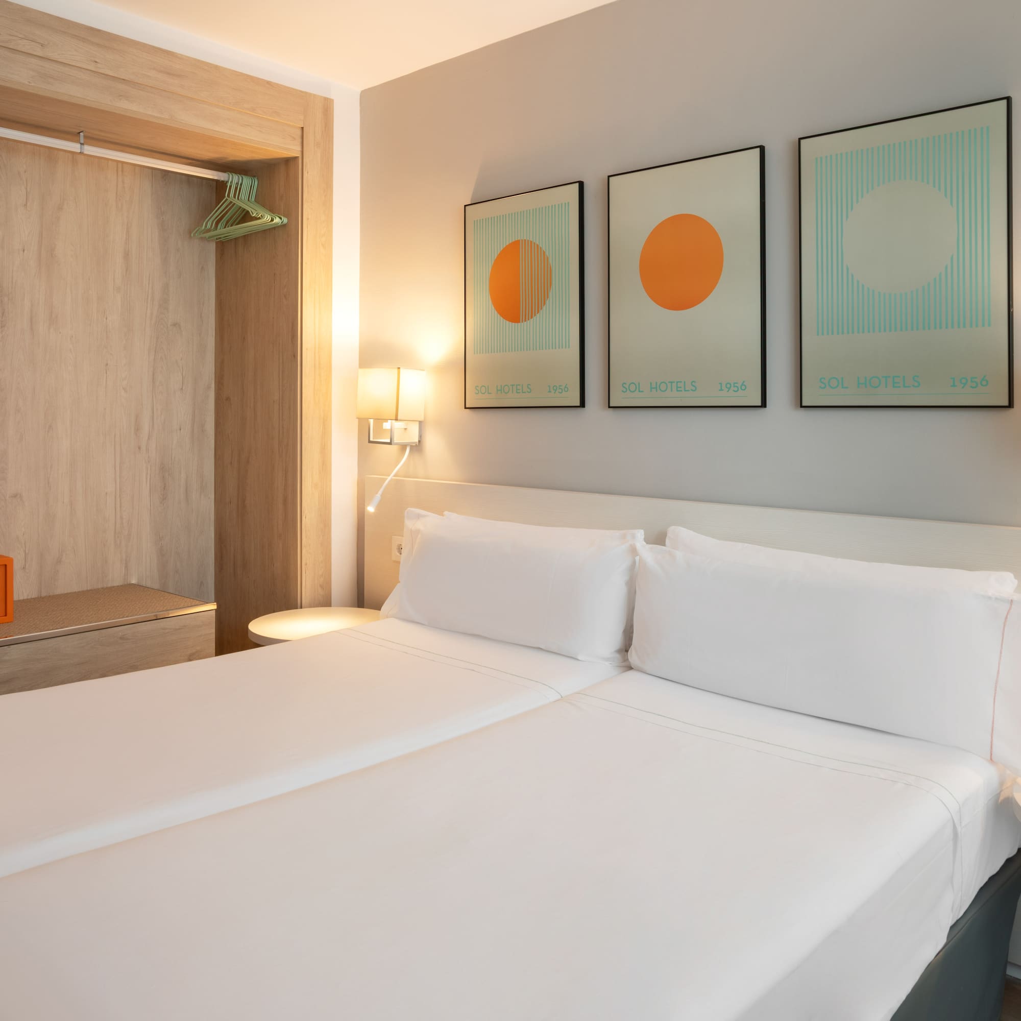 Modern hotel bedroom with twin beds, safe, and Sol Hotels artwork.