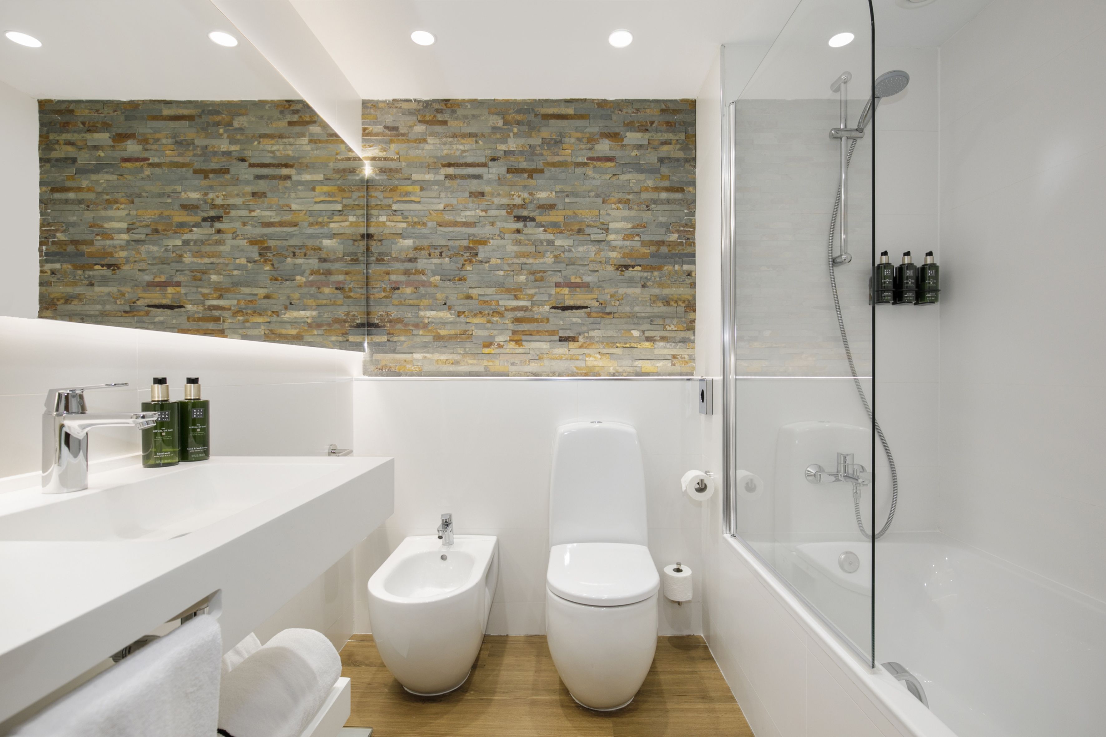 Sleek modern bathroom with stone accent wall, white fixtures, shower, and bidet.