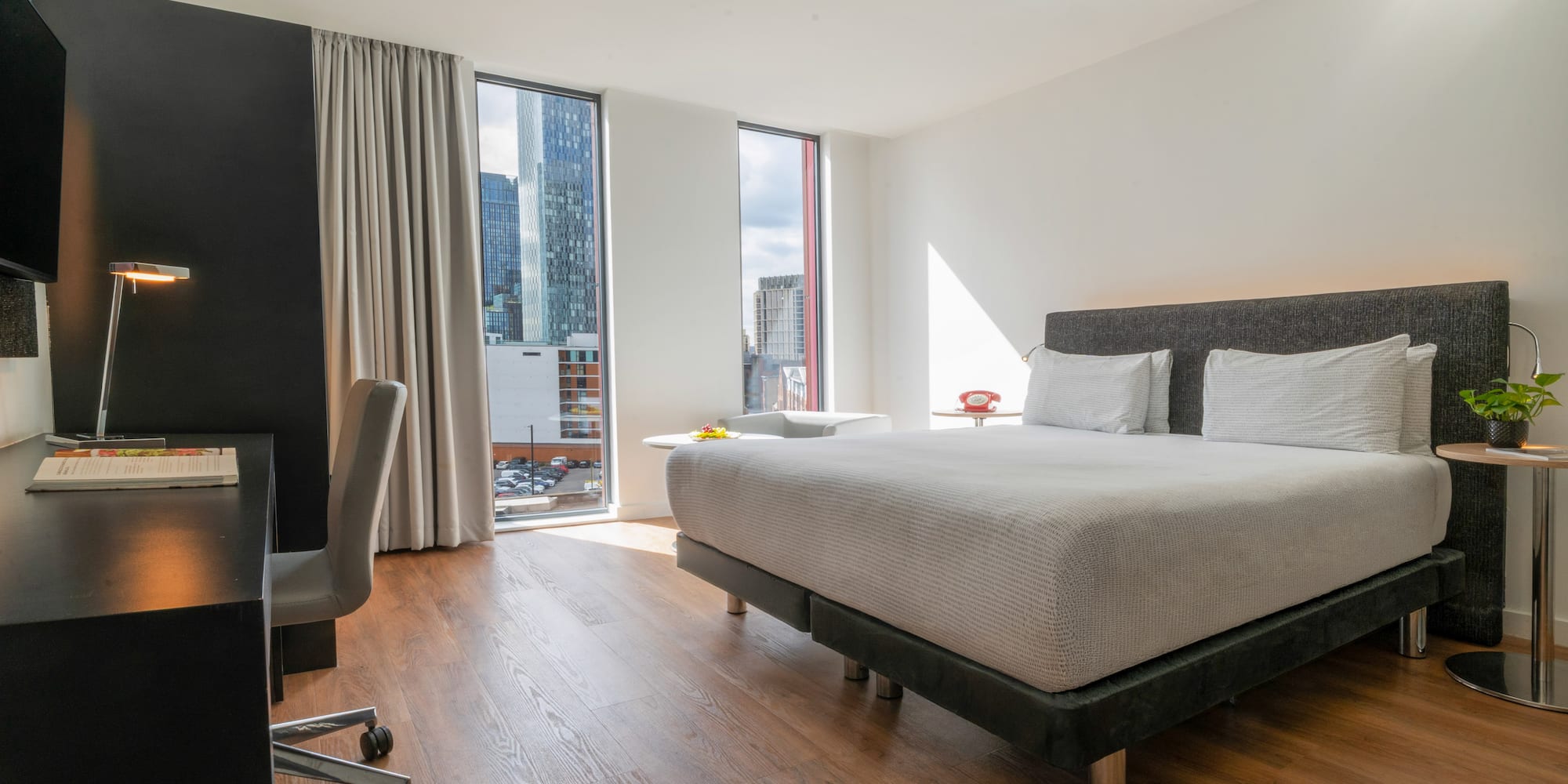 Modern hotel room with city view, bed, and desk.